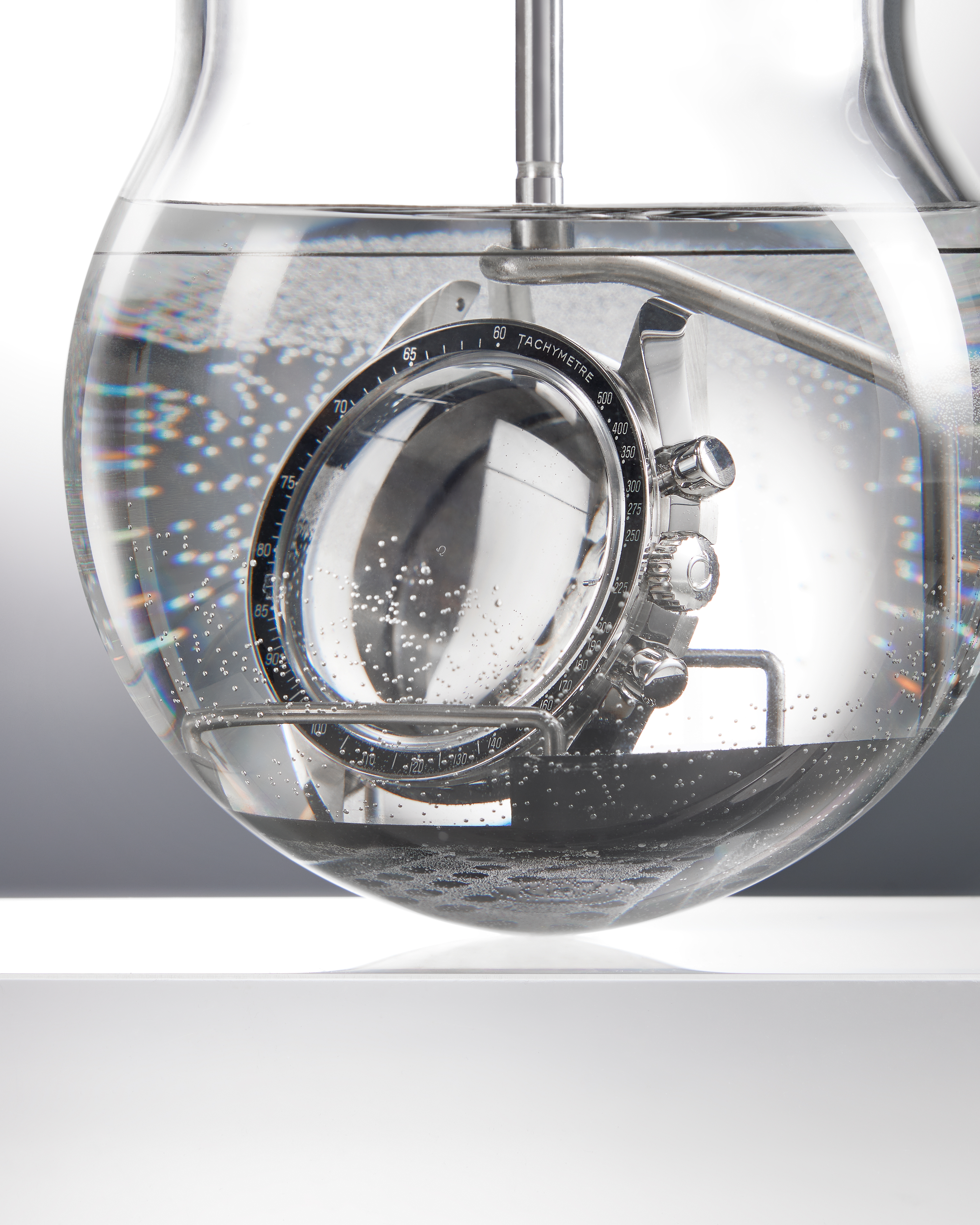 A silver watch with a black bezel submerged in a glass orb filled with water and bubbles.