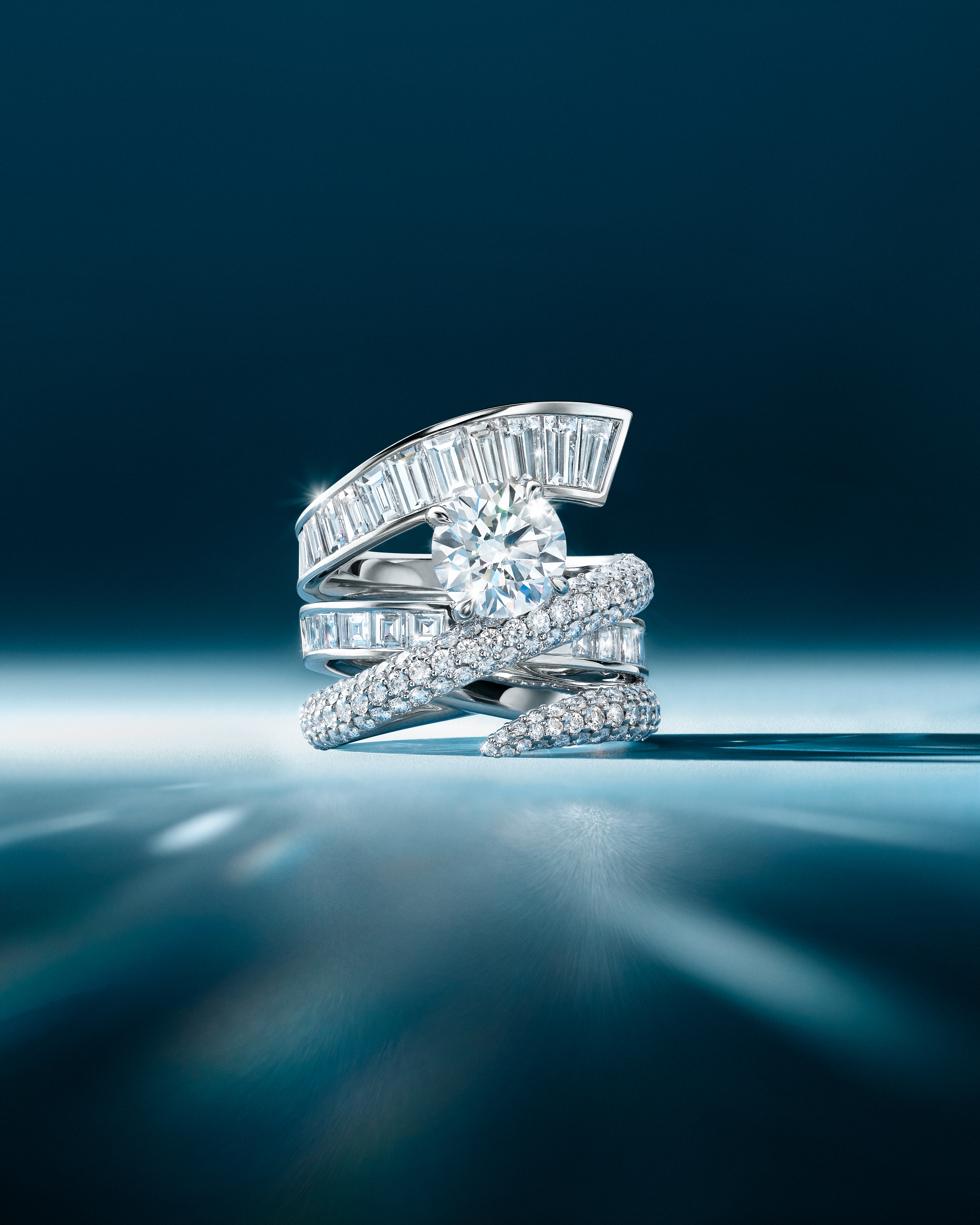 A diamond ring with a large round center stone, surrounded by baguette and pavé diamonds on a swirling platinum band.