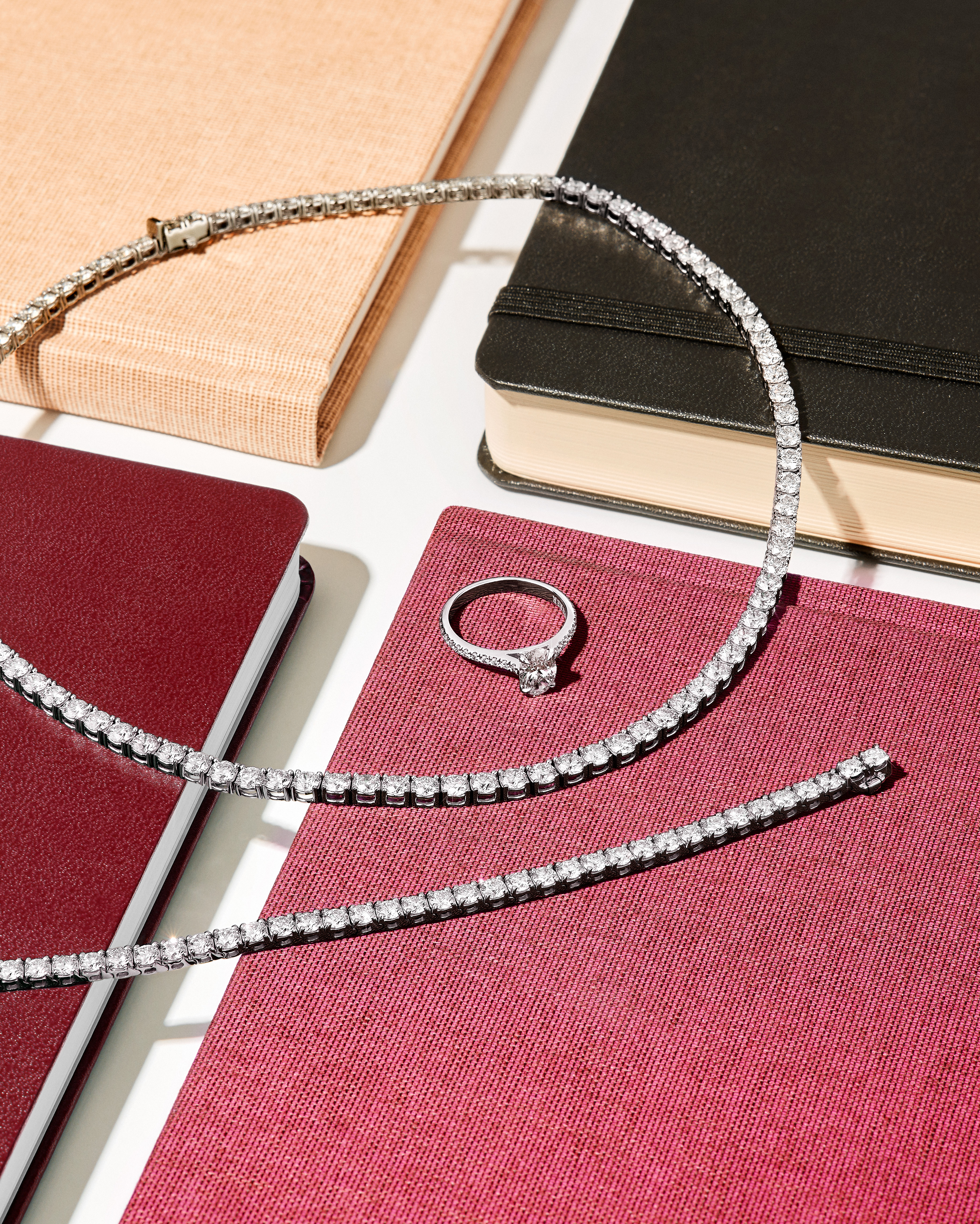 Diamond tennis necklace, bracelet, and ring on notebooks.