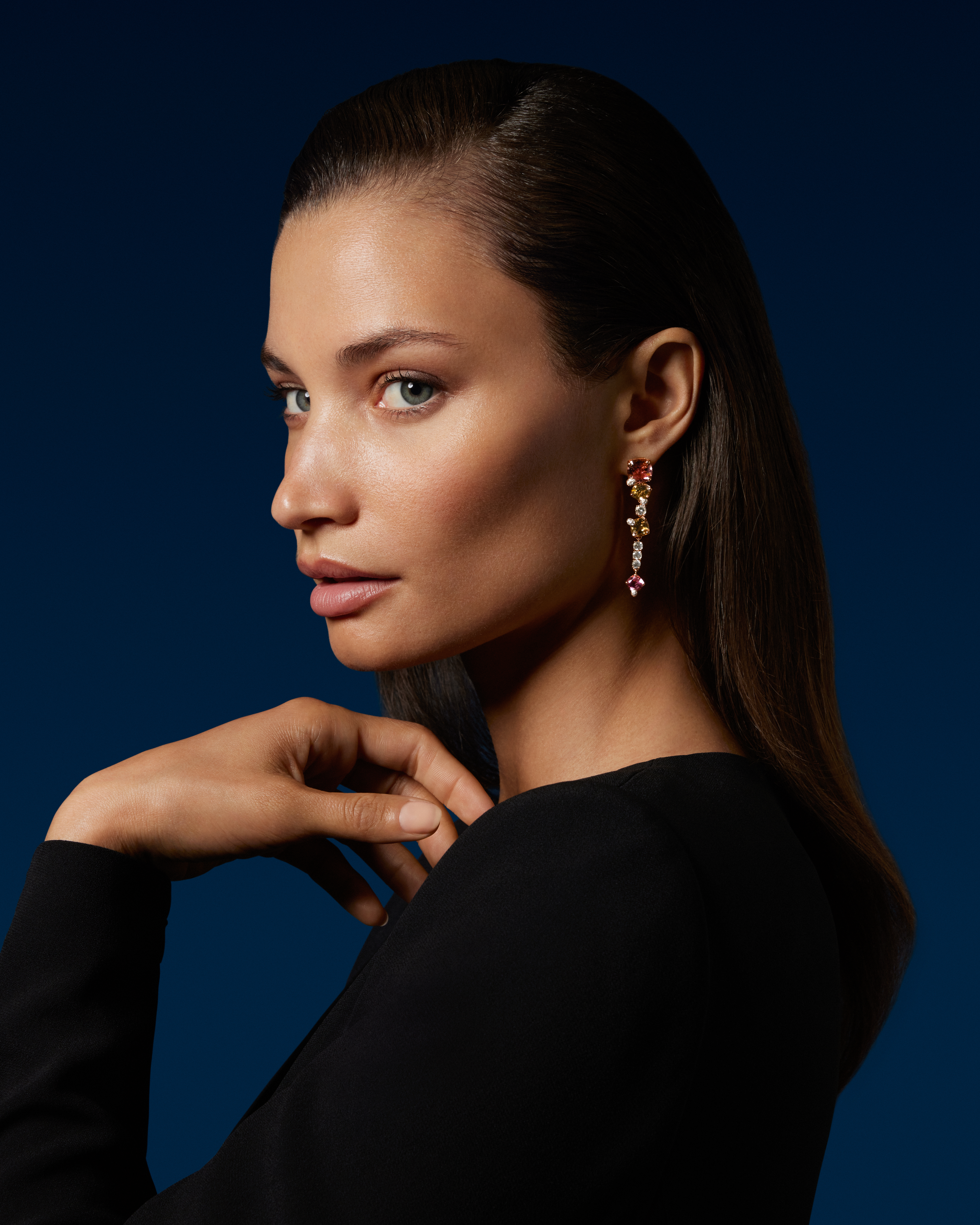 Woman with dark hair and a black top, wearing a colorful gemstone earring, looking left.