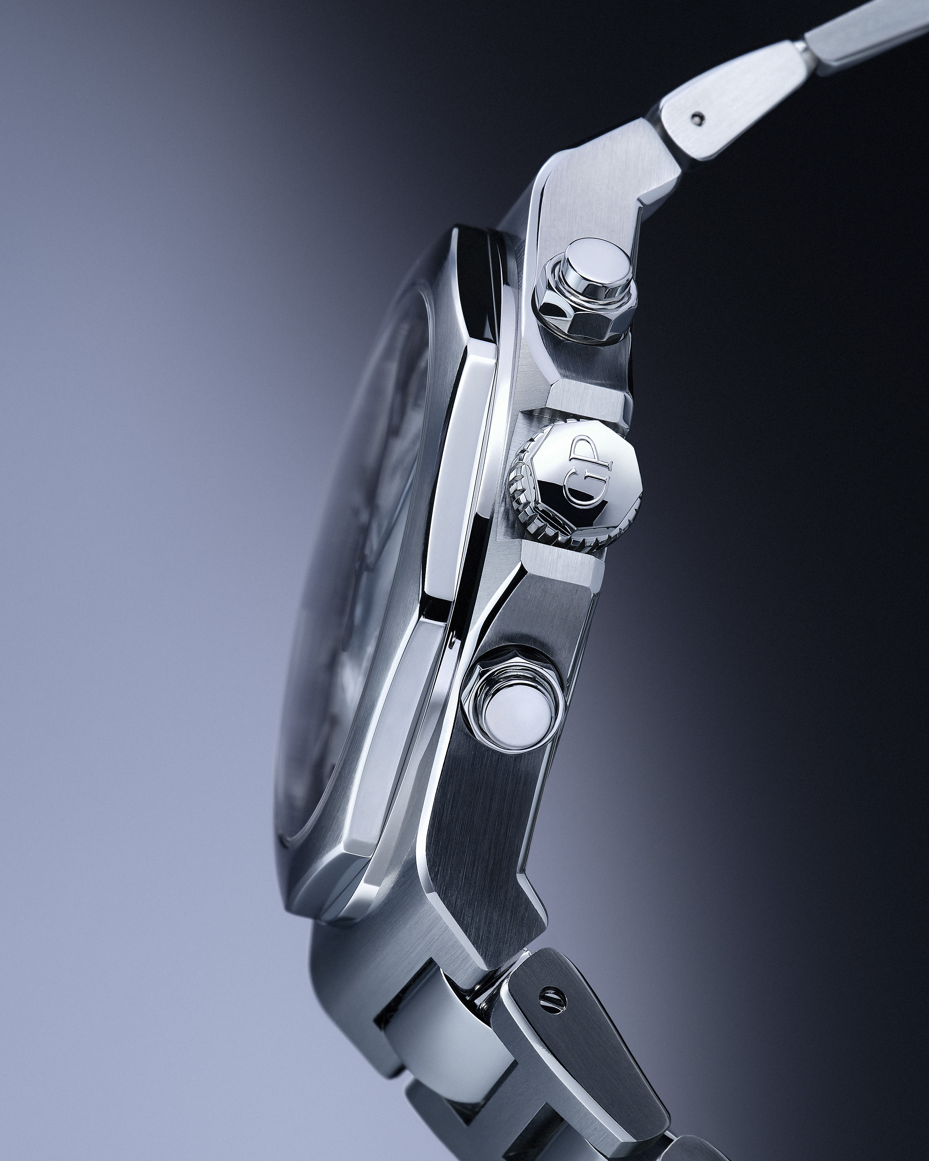 Side view of a silver metal watch with a textured crown and two pushers, against a gradient background.