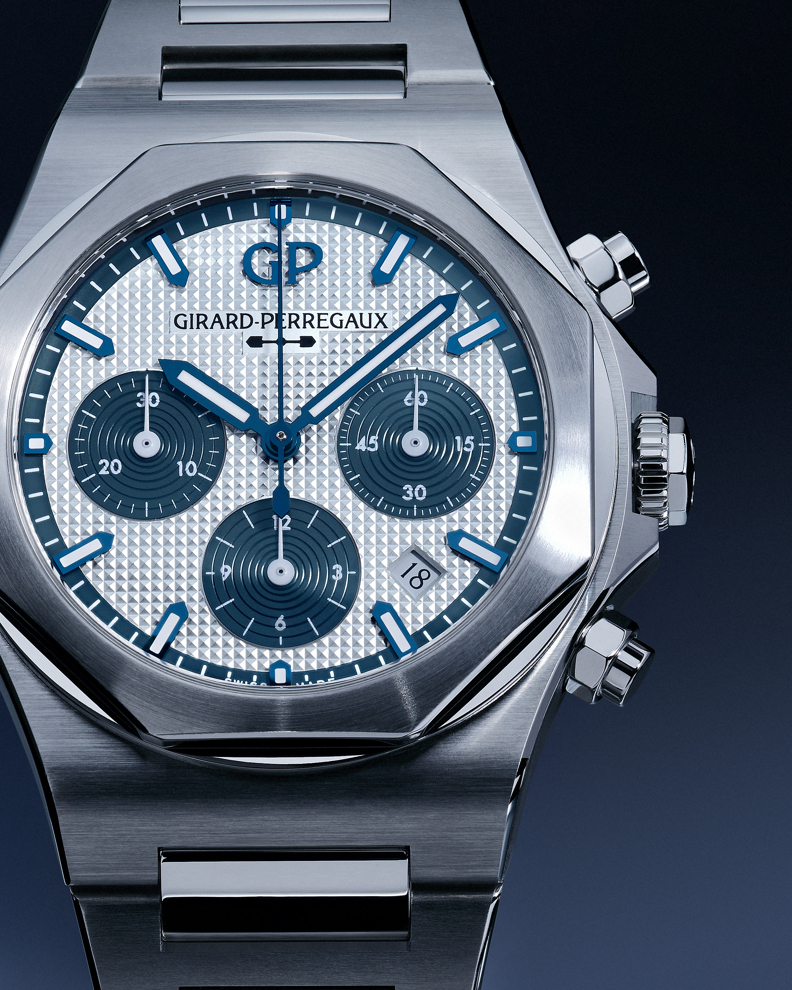A close-up of a silver Girard-Perregaux watch with a textured white face, blue hands, and three subdials.