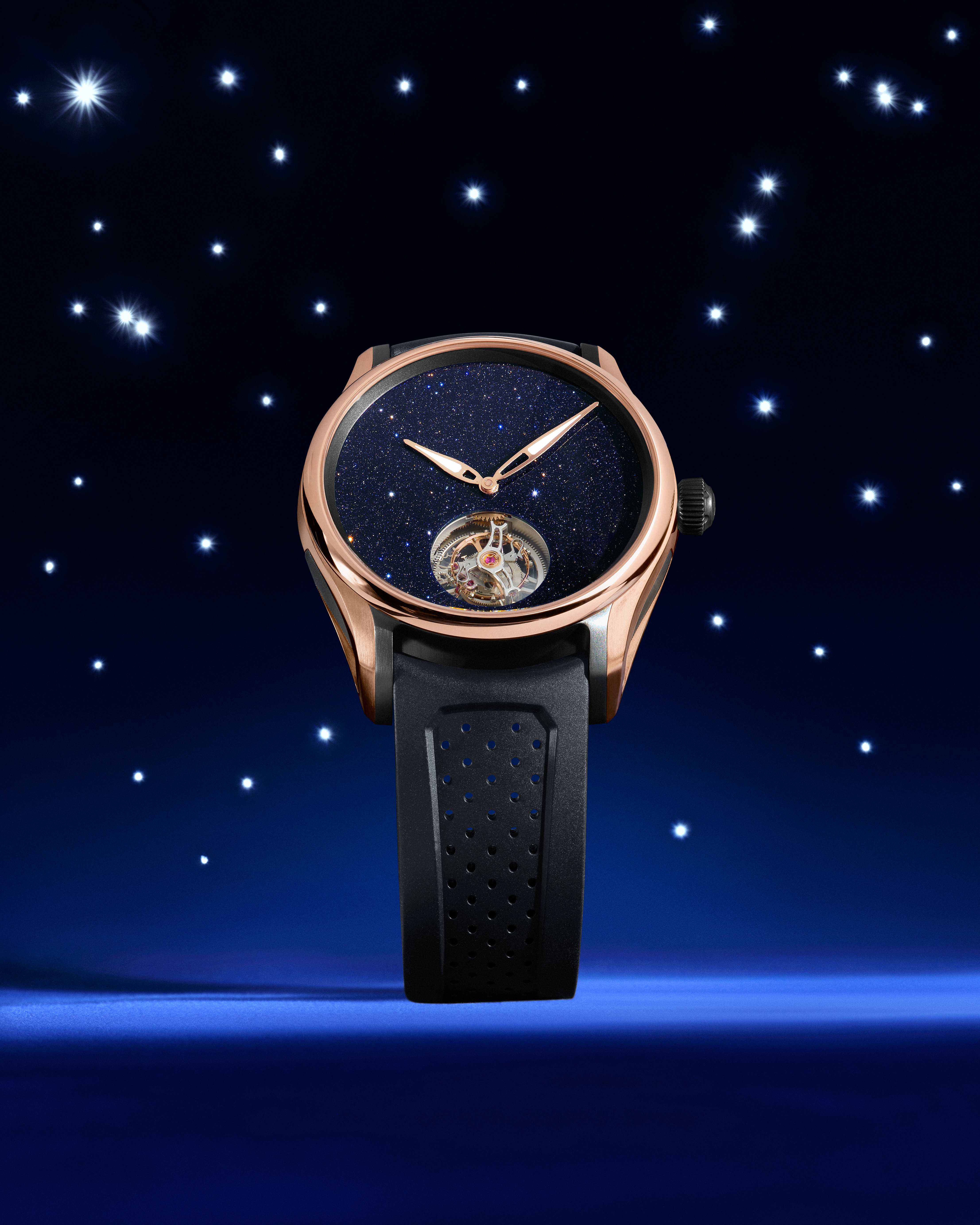 Rose gold watch with a blue glitter dial and exposed tourbillon, on a dark blue background with stars.
