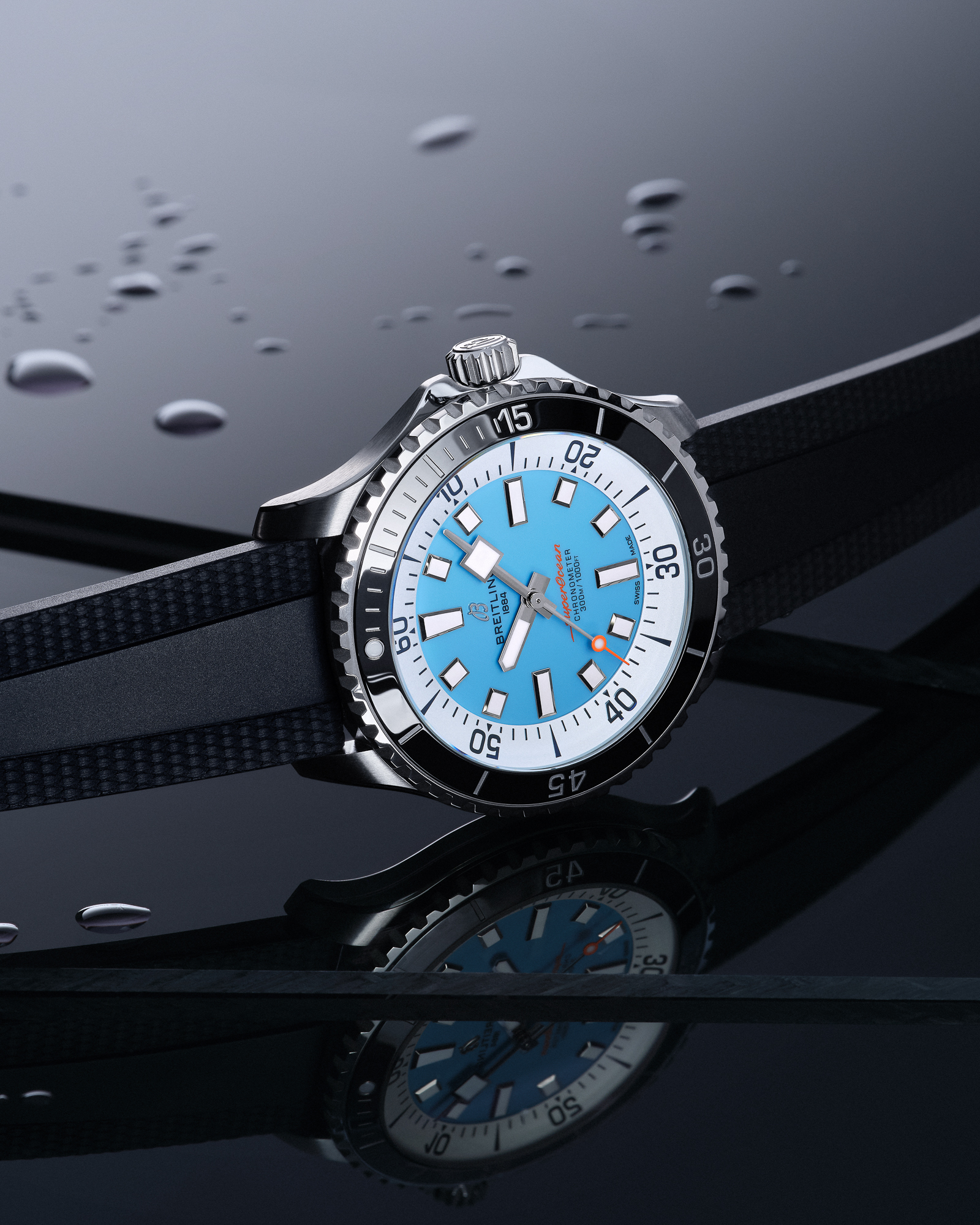 A Breitling Superocean Chronometer watch with a light blue face, black bezel, and black rubber strap, on a wet, reflective black surface.