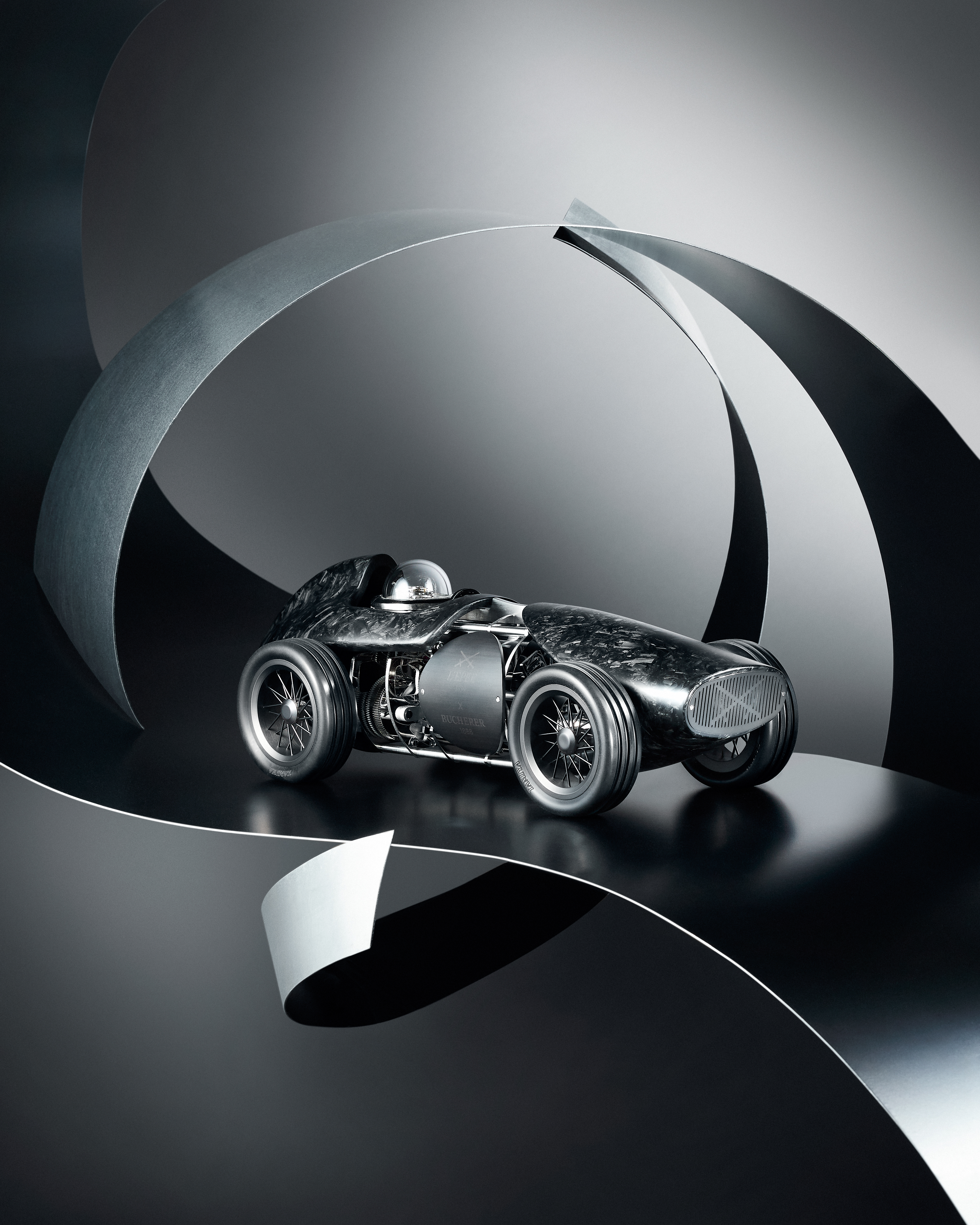 A sleek, dark gray, futuristic race car with exposed engine components, set against a backdrop of curved metallic panels.