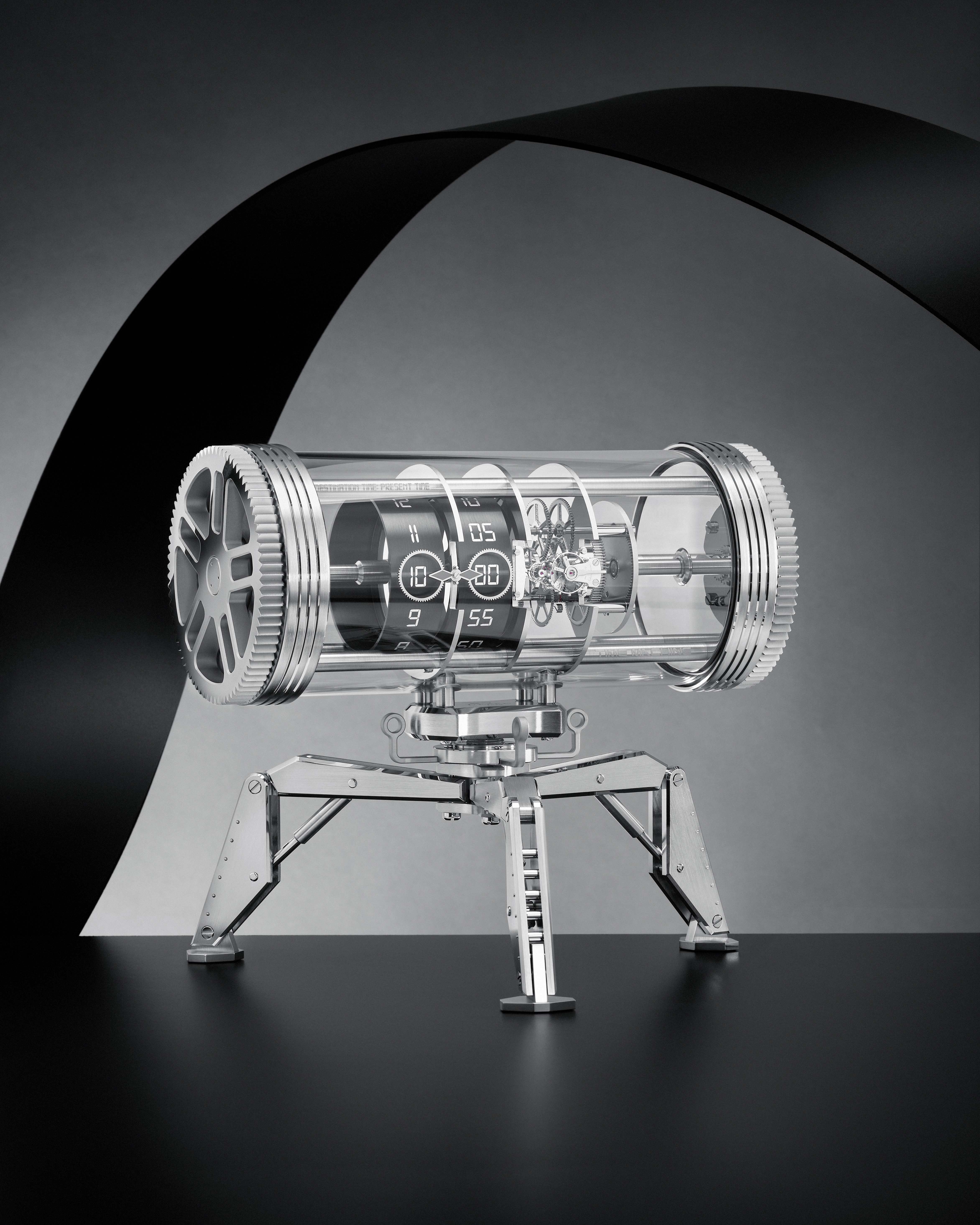 A cylindrical, clear glass clock with exposed gears and a digital display, mounted on a chrome tripod stand.