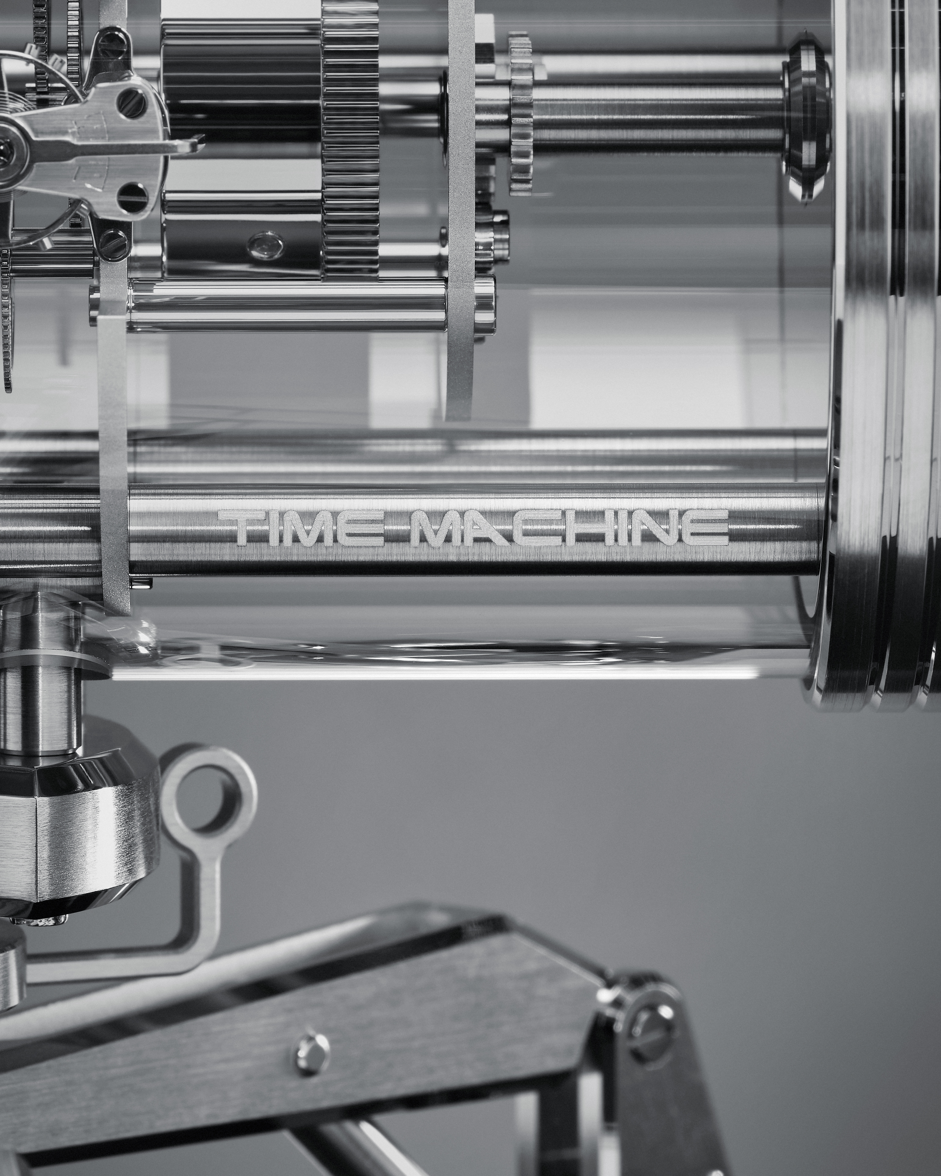 Nahaufnahme einer metallischen Inschrift „ZEITMASCHINE“ auf einem zylindrischen Bauteil, umgeben von Zahnrädern und mechanischen Teilen.