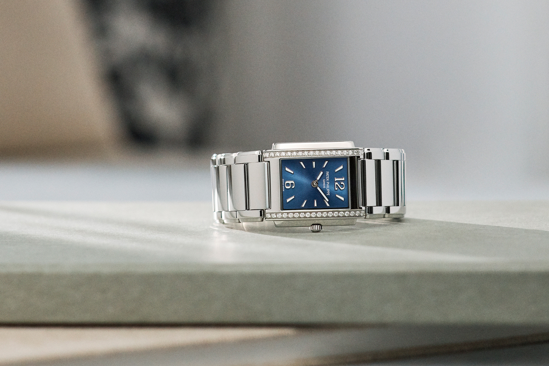 Silver rectangular watch with a blue face and diamond-studded bezel.