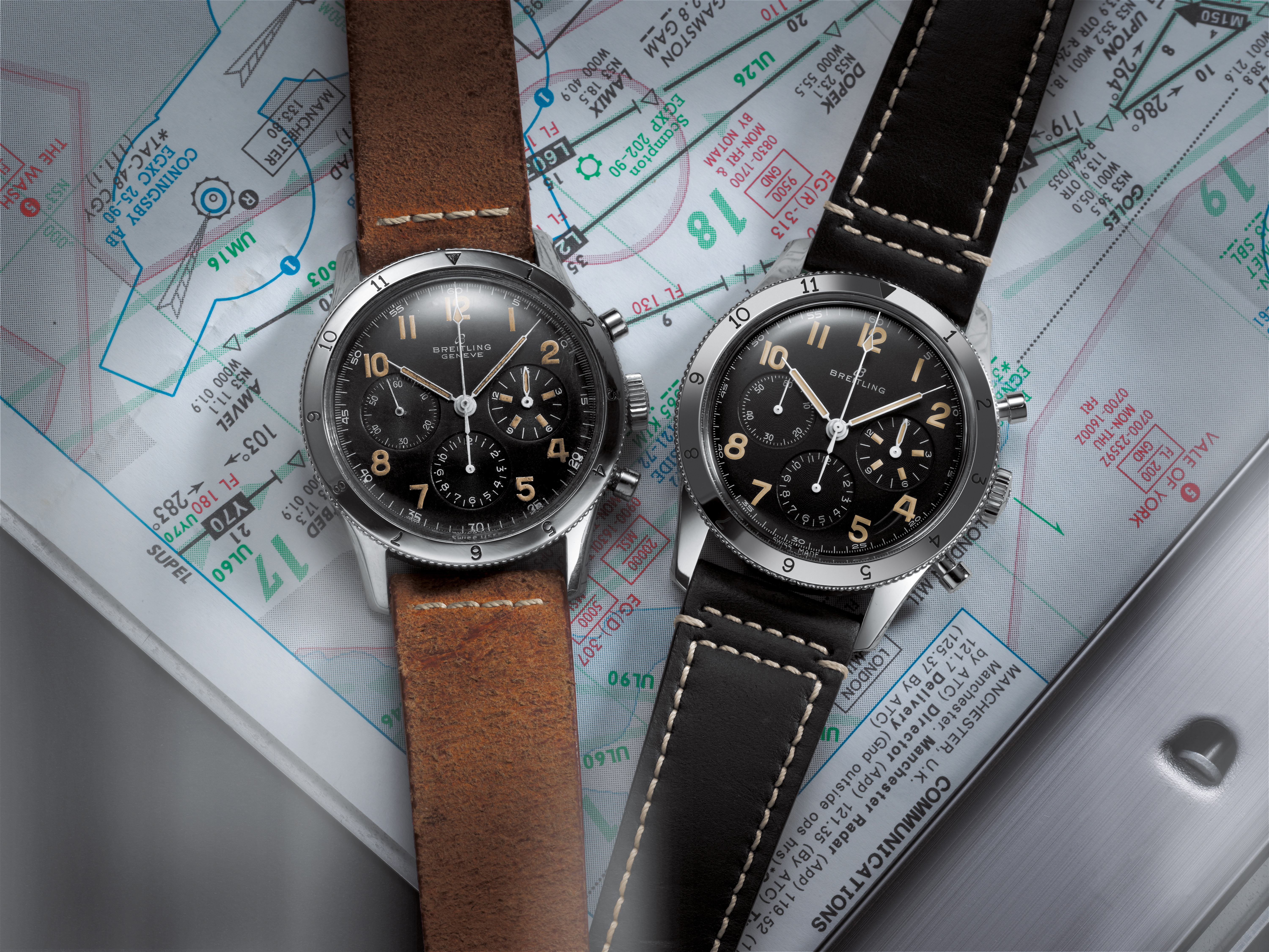 Two Breitling Avi watches with a stainless steel case, black dial, gold numerals and a black and brown leather strap lie on a card.