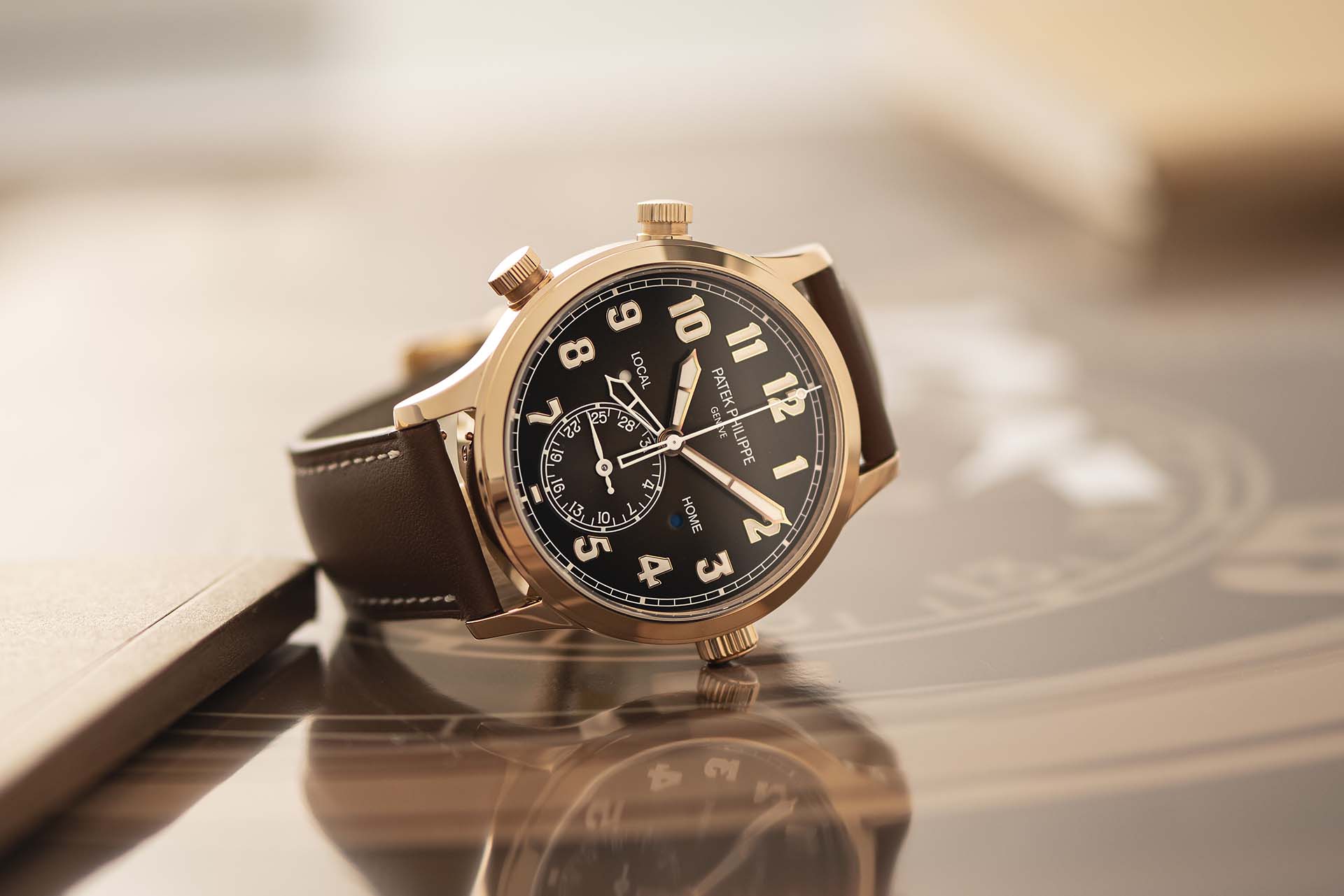 A gold Patek Philippe watch with a black face, white numerals, and a brown leather strap.