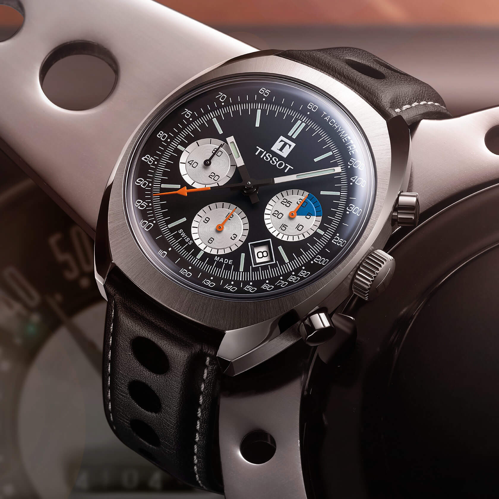 Une montre chronographe Tissot avec un cadran noir, des sous-cadrans argentés et un bracelet en cuir noir perforé.