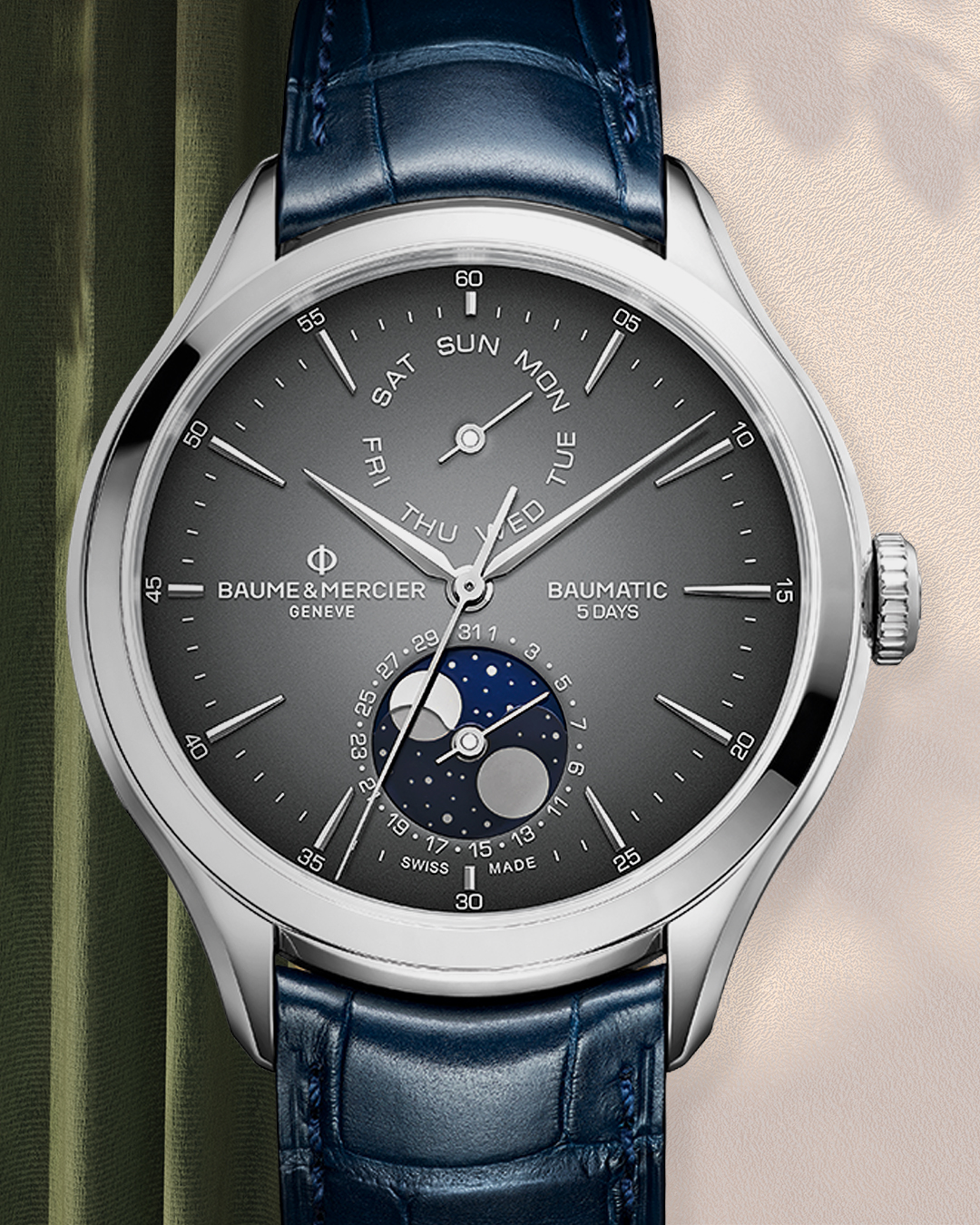 A silver watch with a dark gray face, blue leather strap, and moon phase indicator.