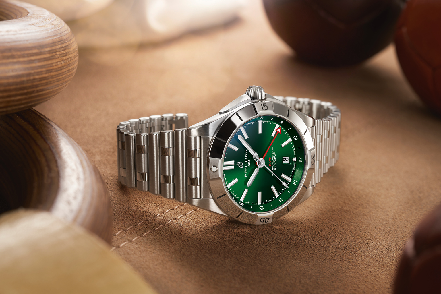 A Breitling “Chronomat GMT” with a green dial and a steel bracelet on a brown surface.