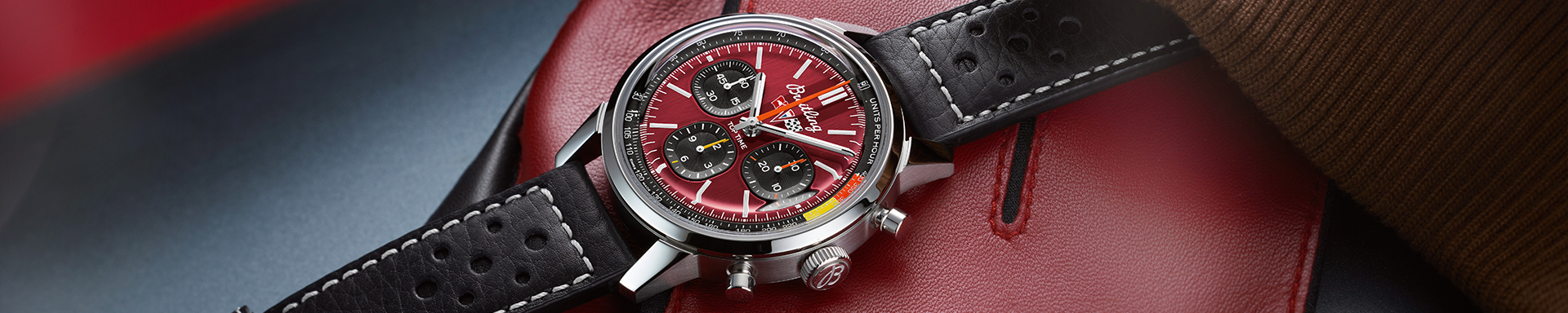 A Breitling “Top Time B01 Corvette” with a black leather strap, red dial and seconds display on a red background.