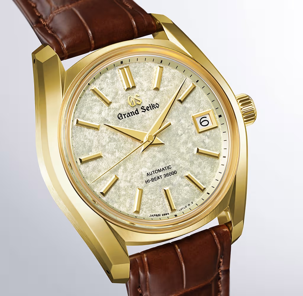 Eine goldene Grand Seiko Uhr mit strukturiertem weißen Zifferblatt, goldenen Zeigern und braunem Lederarmband.