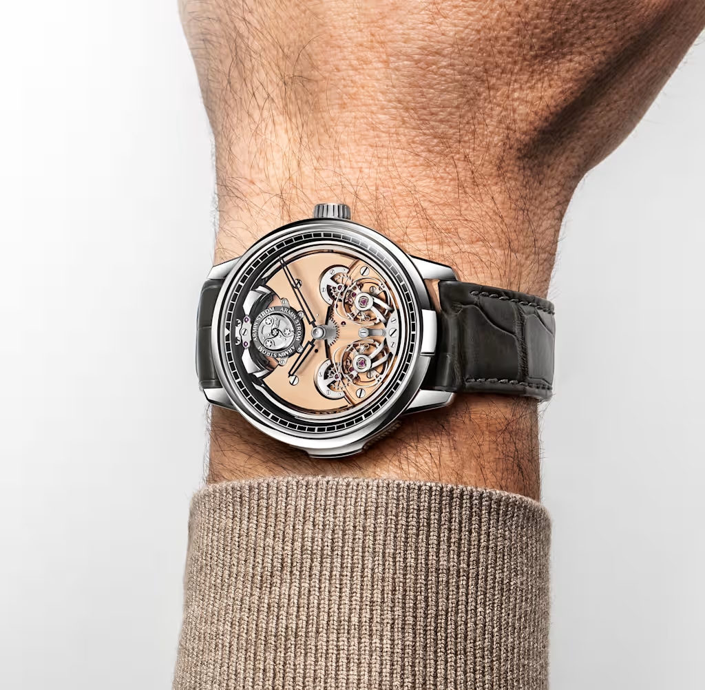 Das Handgelenk eines Mannes, der eine silberne Uhr mit freiliegendem mechanischem Uhrwerk und einem dunklen Alligatorlederarmband trägt.
