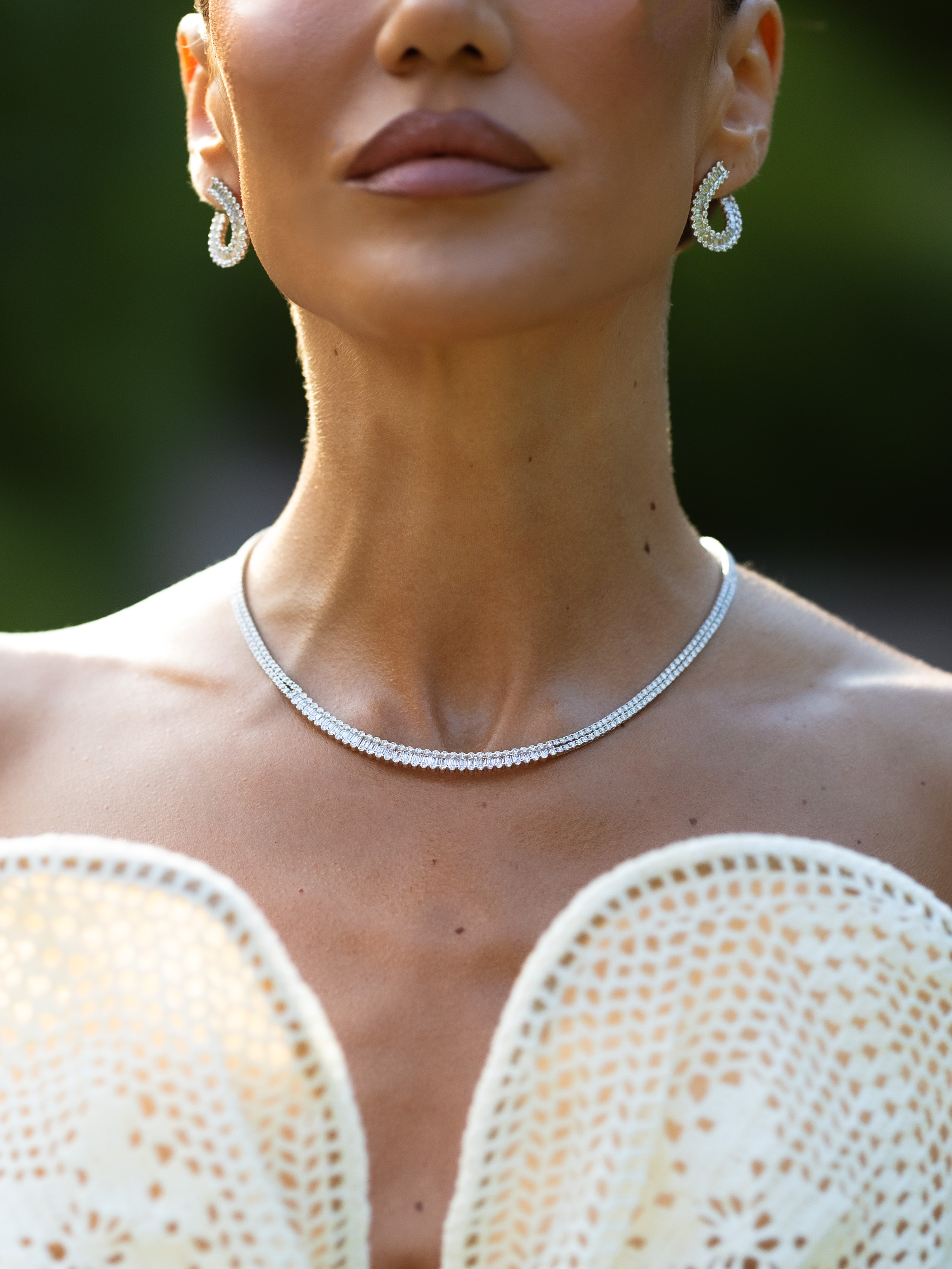 Eine Frau, die eine Diamantkette und dazu passende Ohrringe trägt, dazu ein weißes Häkeltop.