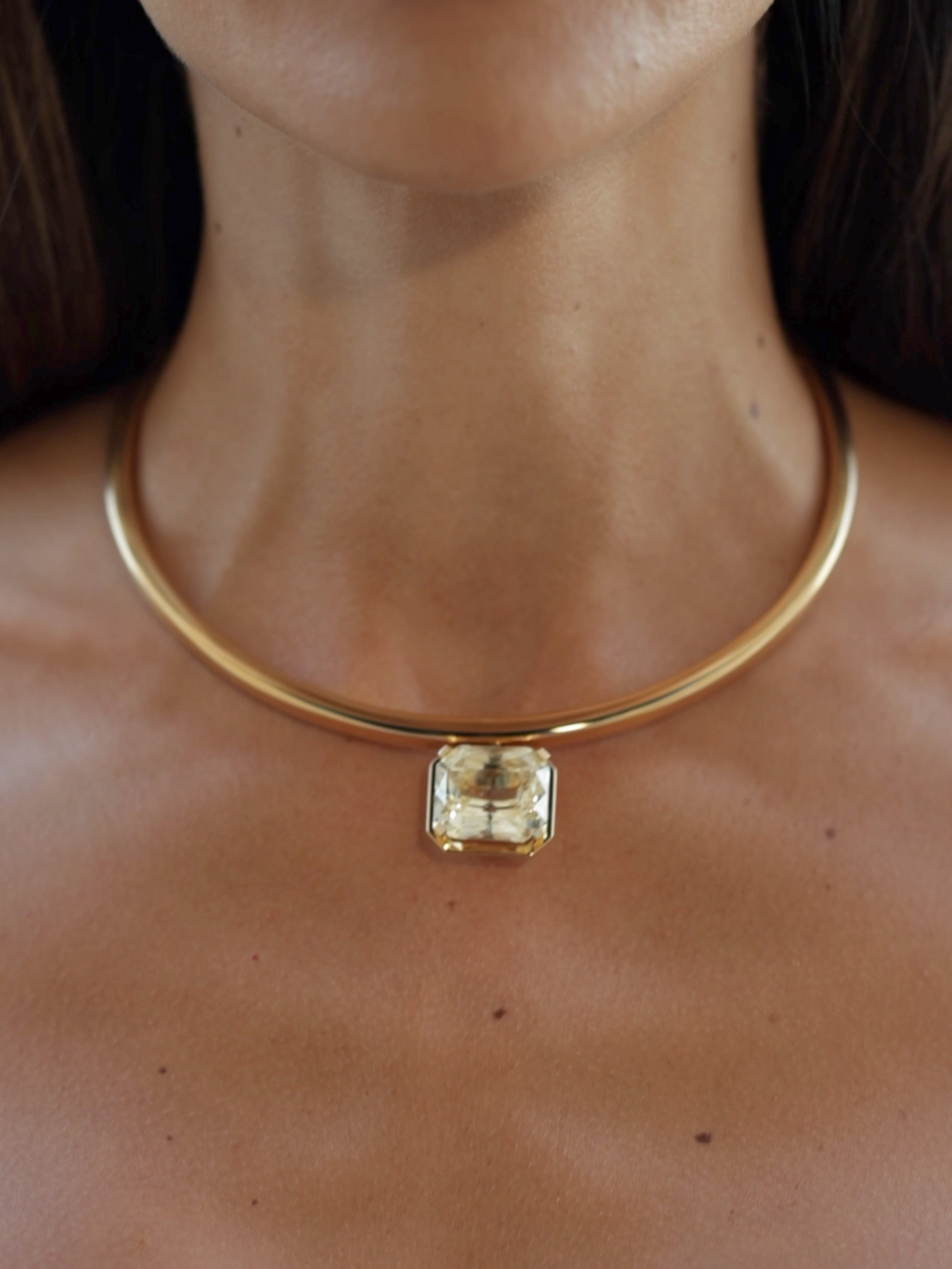 Eine Frau trägt eine goldene Choker-Halskette mit einem großen, rechteckigen gelben Edelsteinanhänger.