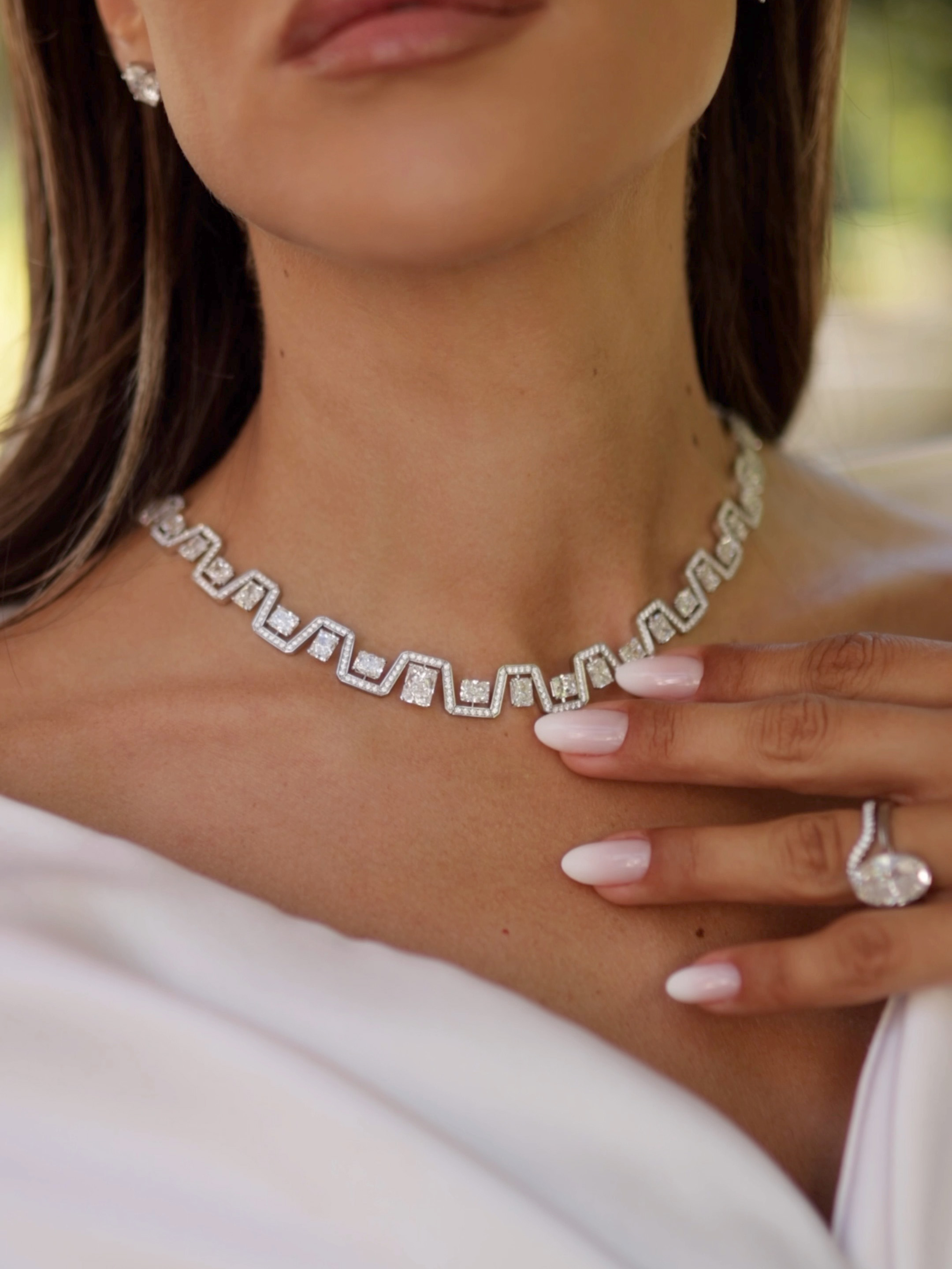Eine Frau, die eine Diamantkette mit geometrischen Mustern, dazu passende Ohrringe und einen großen Diamantring trägt.