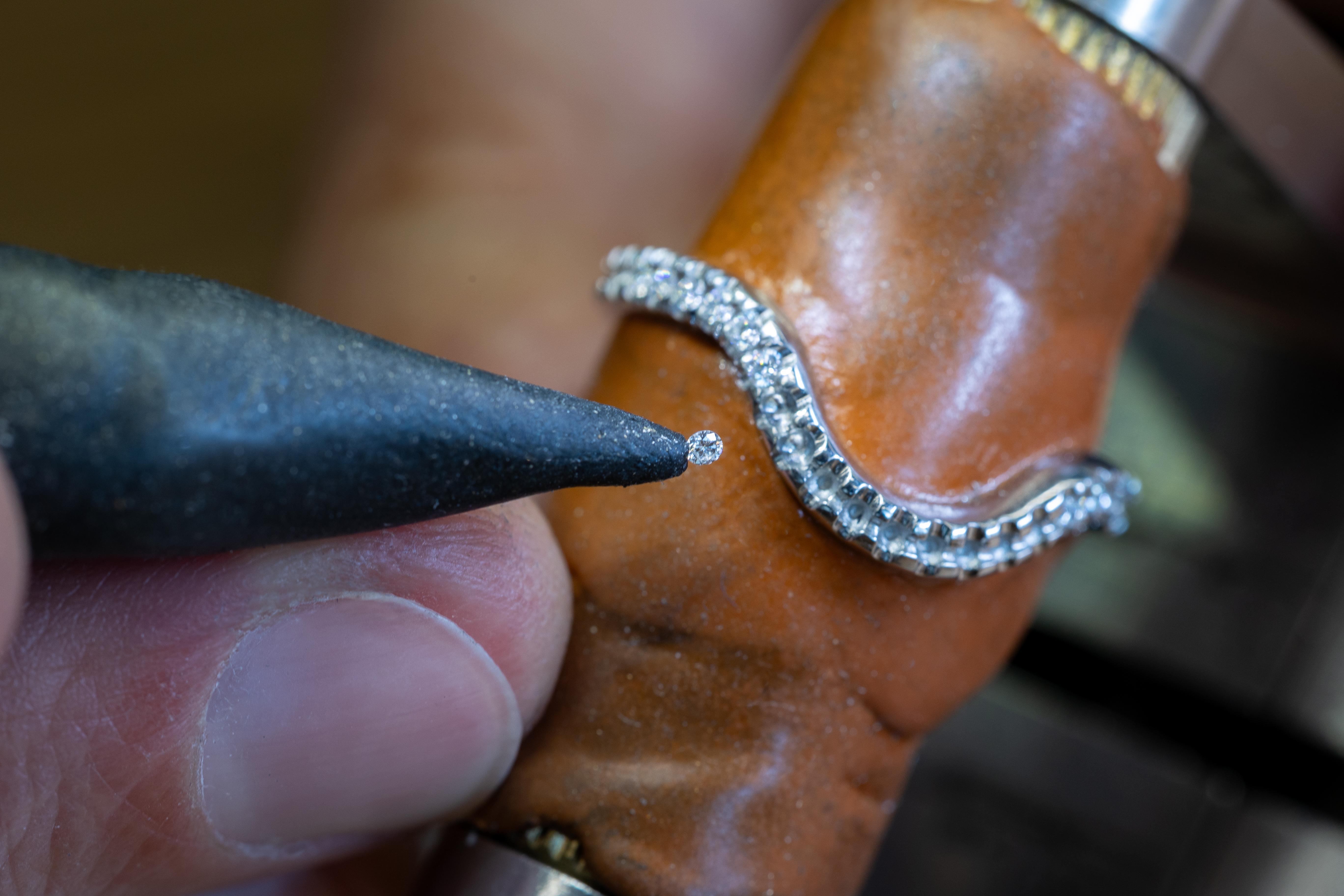 Ein Juwelier fasst mit einem spitzen Werkzeug einen kleinen Diamanten in einen Silberring ein.