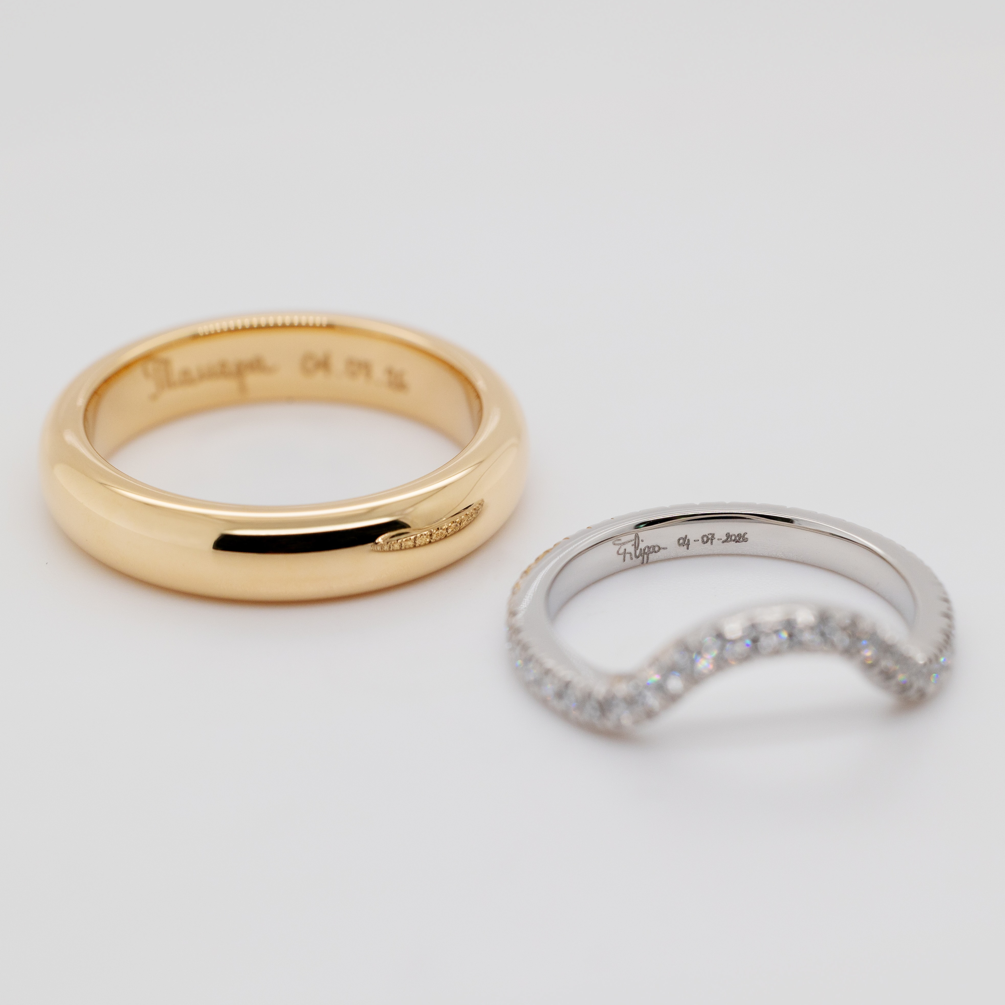 A gold wedding band and a curved silver diamond band, both engraved with names and dates.