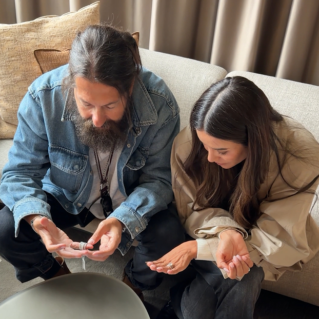 A man with a beard and a woman with long dark hair looking at their hands.