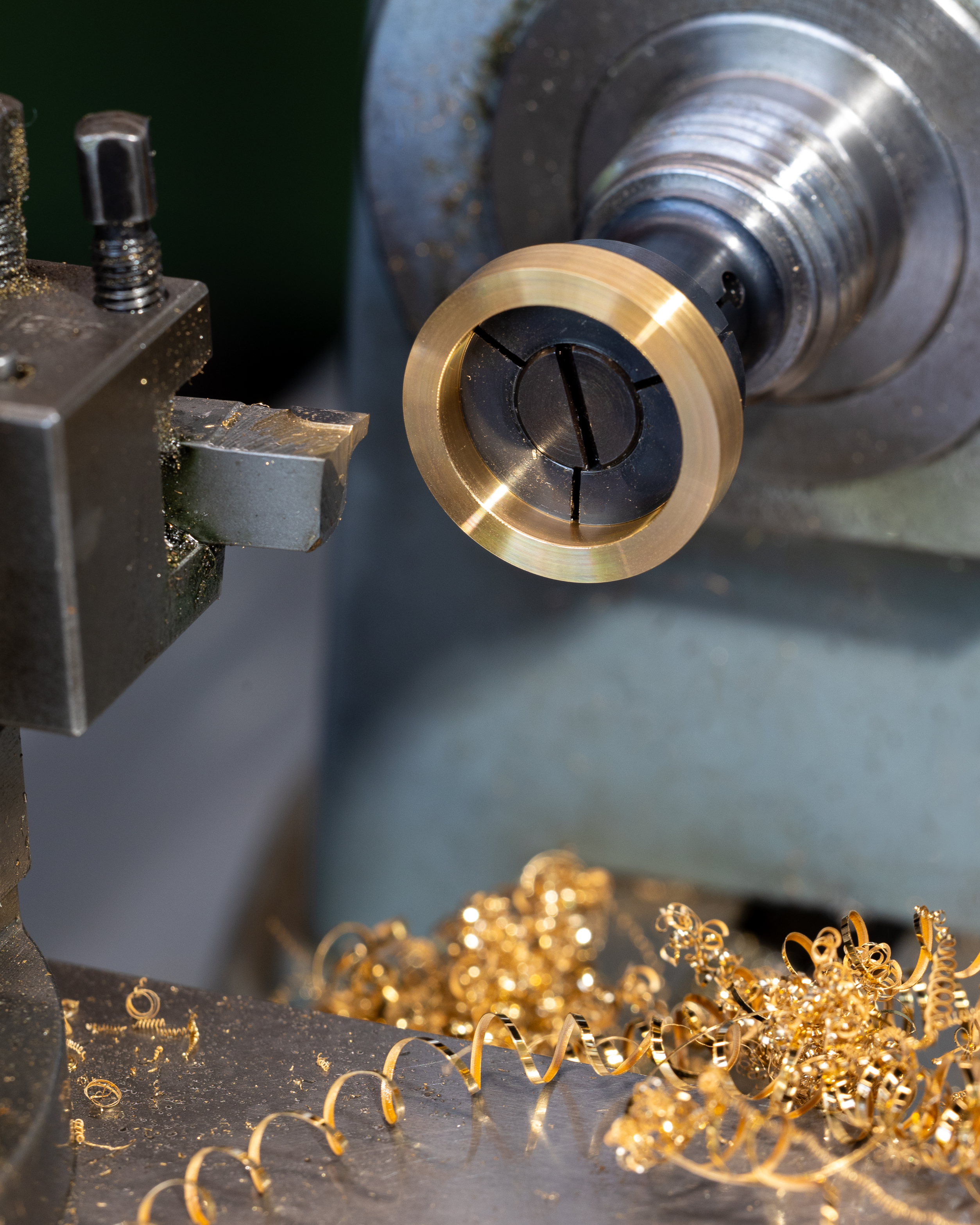 A brass ring being machined on a lathe, with metal shavings on the surface below.