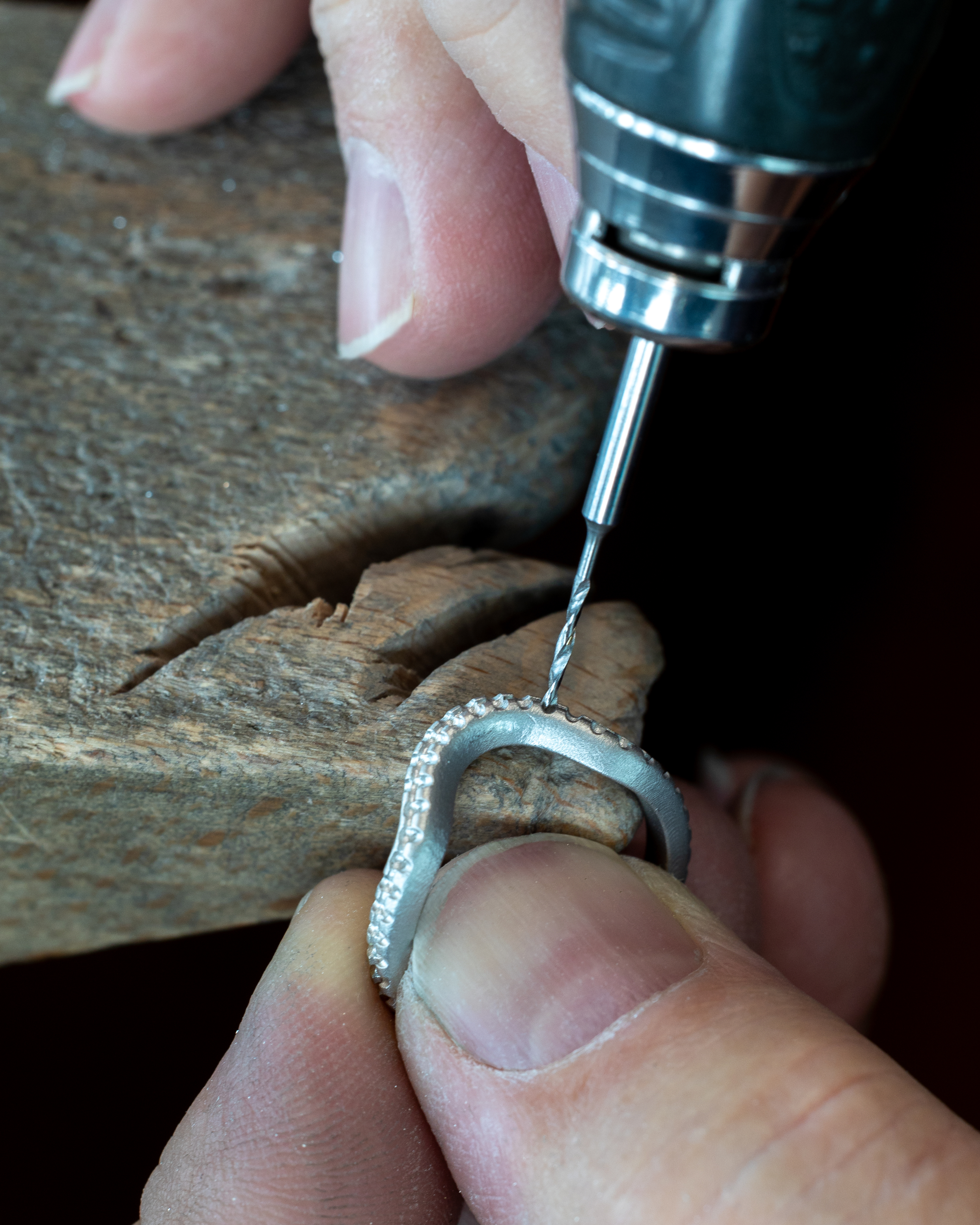A jeweler uses a rotary tool to drill into a silver ring with embedded stones.