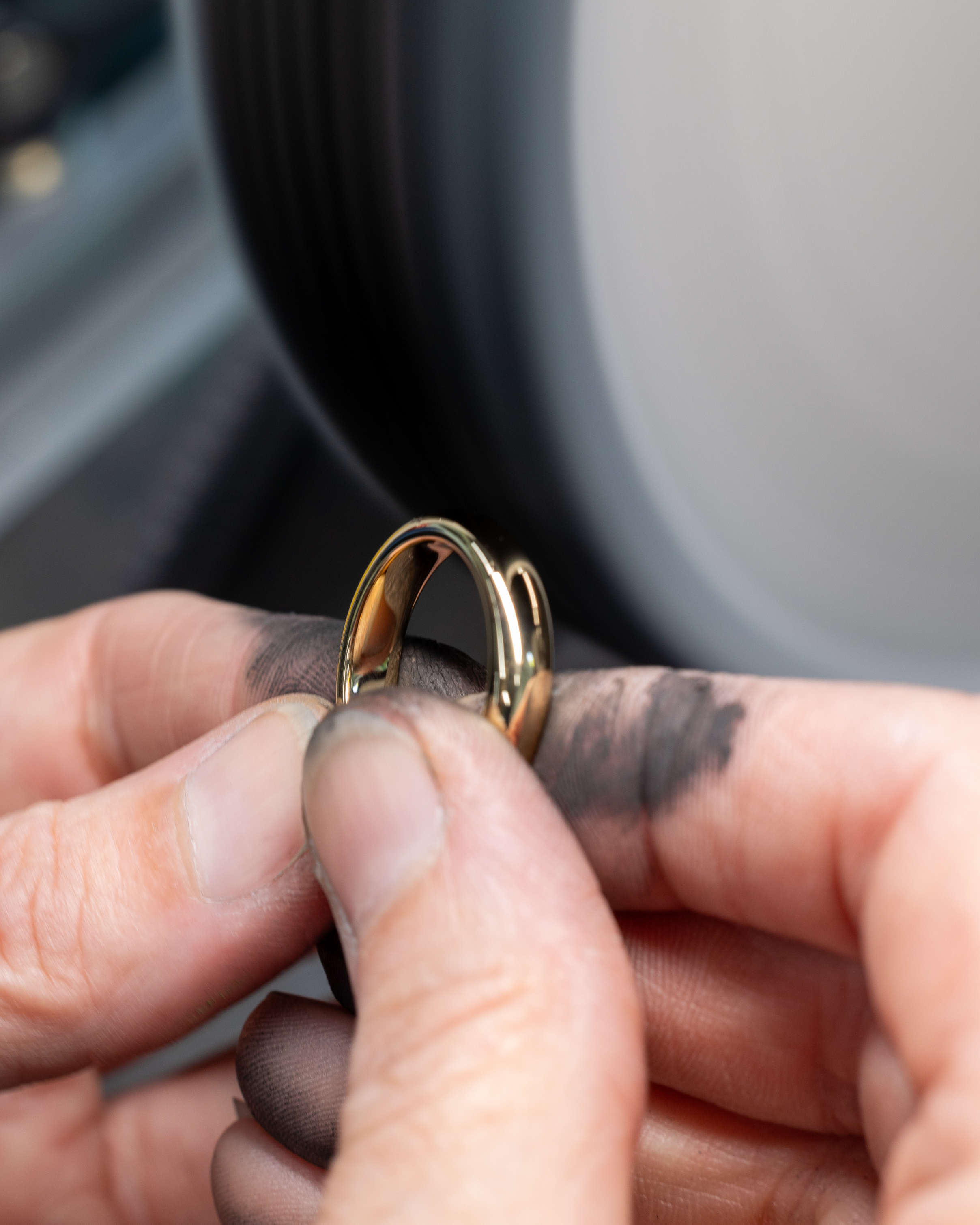 Hands with smudged fingers holding a gold ring against a blurred background.