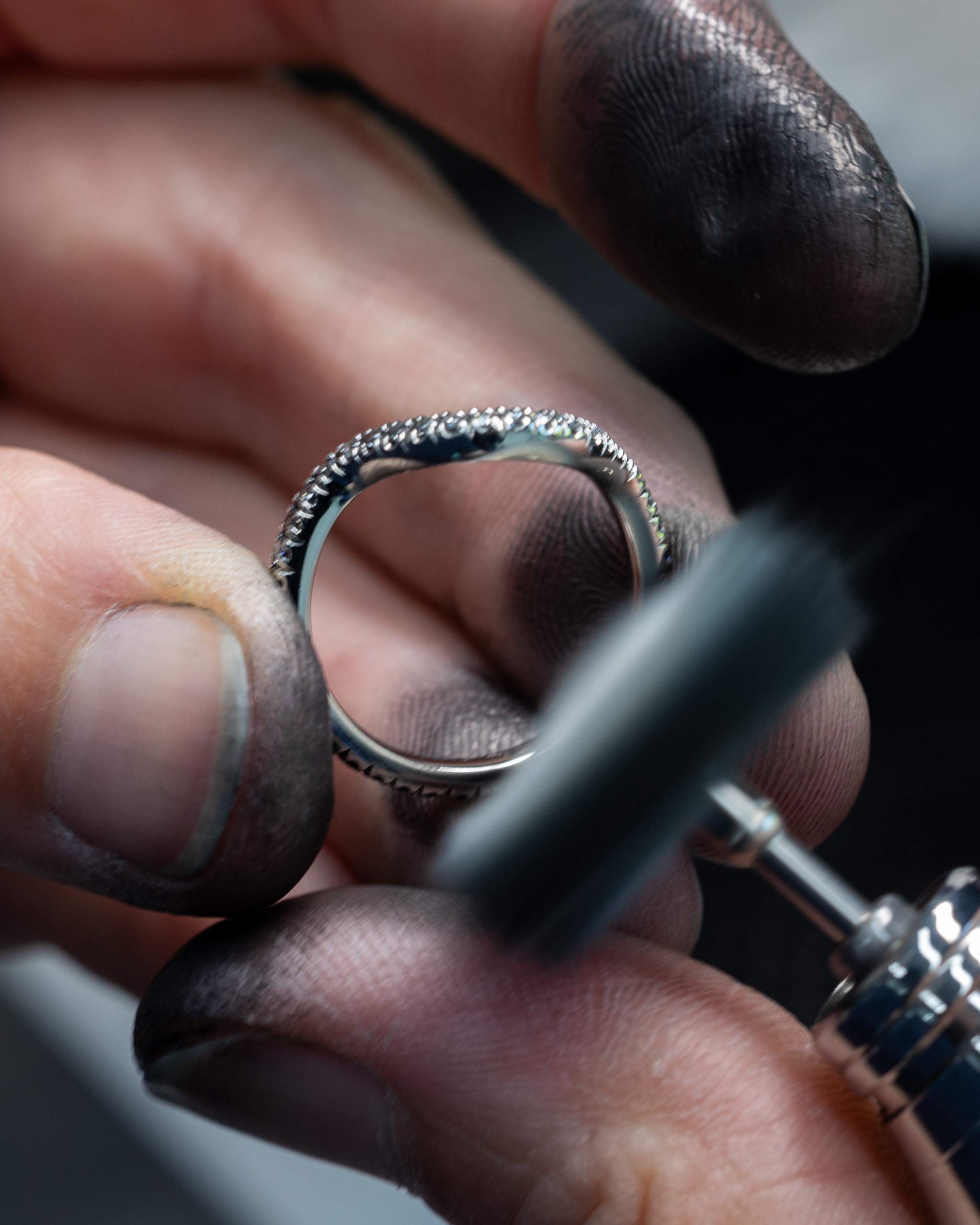 A jeweler's dirty hands hold a diamond ring while polishing it with a rotary tool.