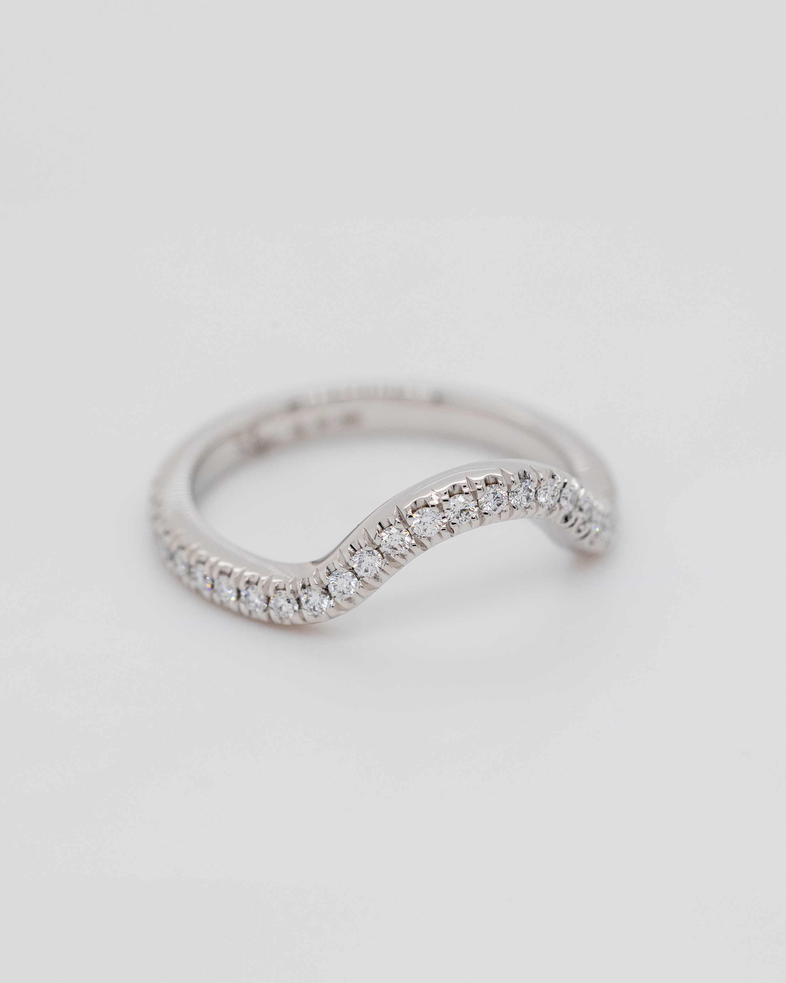A white gold curved wedding band with small diamonds set along the top.