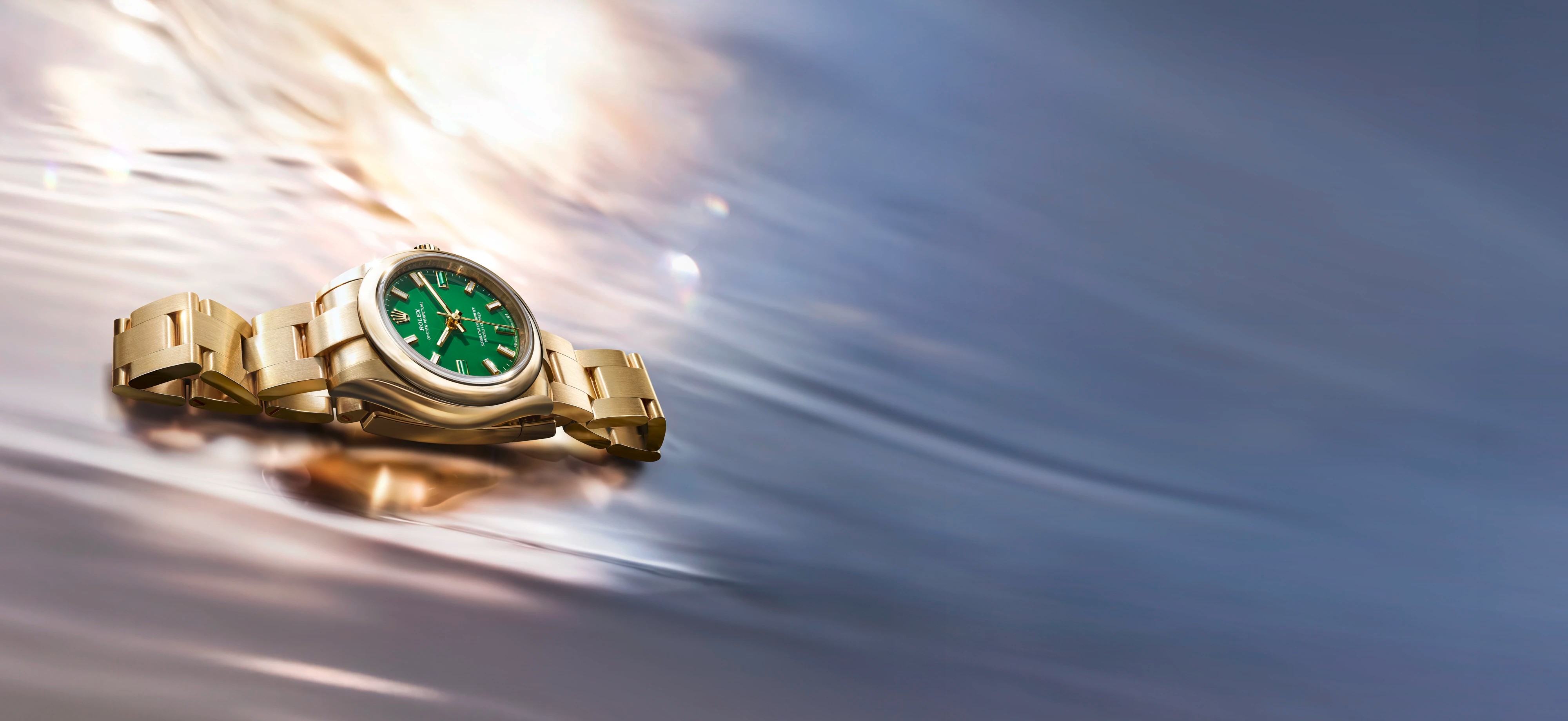 Eine goldene Rolex-Uhr mit grünem Zifferblatt auf einer reflektierenden, wellenförmigen Oberfläche mit warmen und kühlen Farbtönen.
