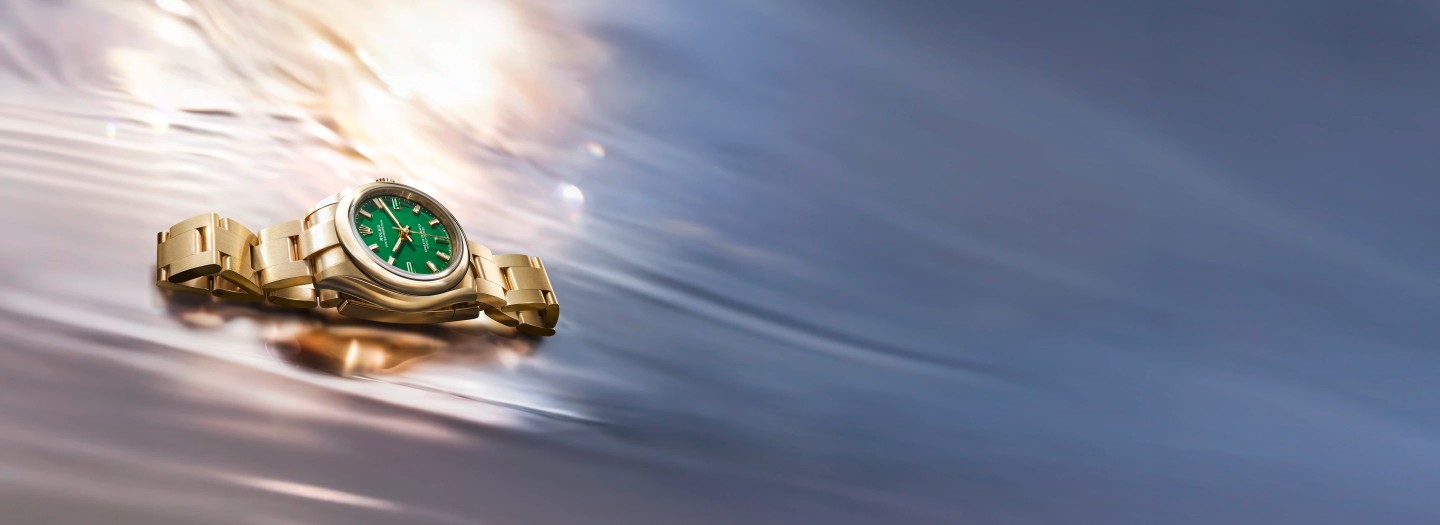 A gold Rolex watch with a green face submerged in rippling water.