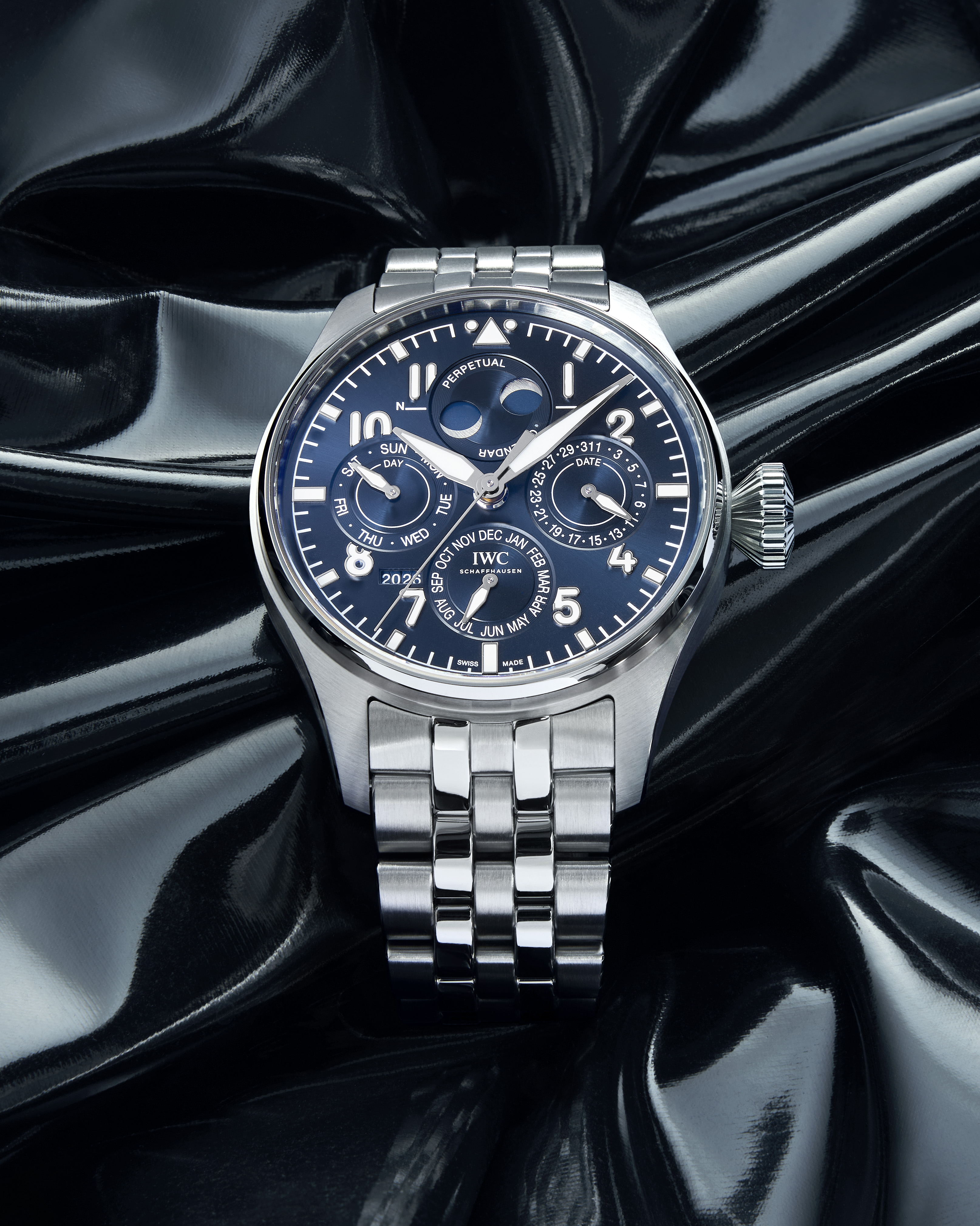 A silver IWC Schaffhausen watch with a blue face and multiple subdials, resting on a reflective black surface.