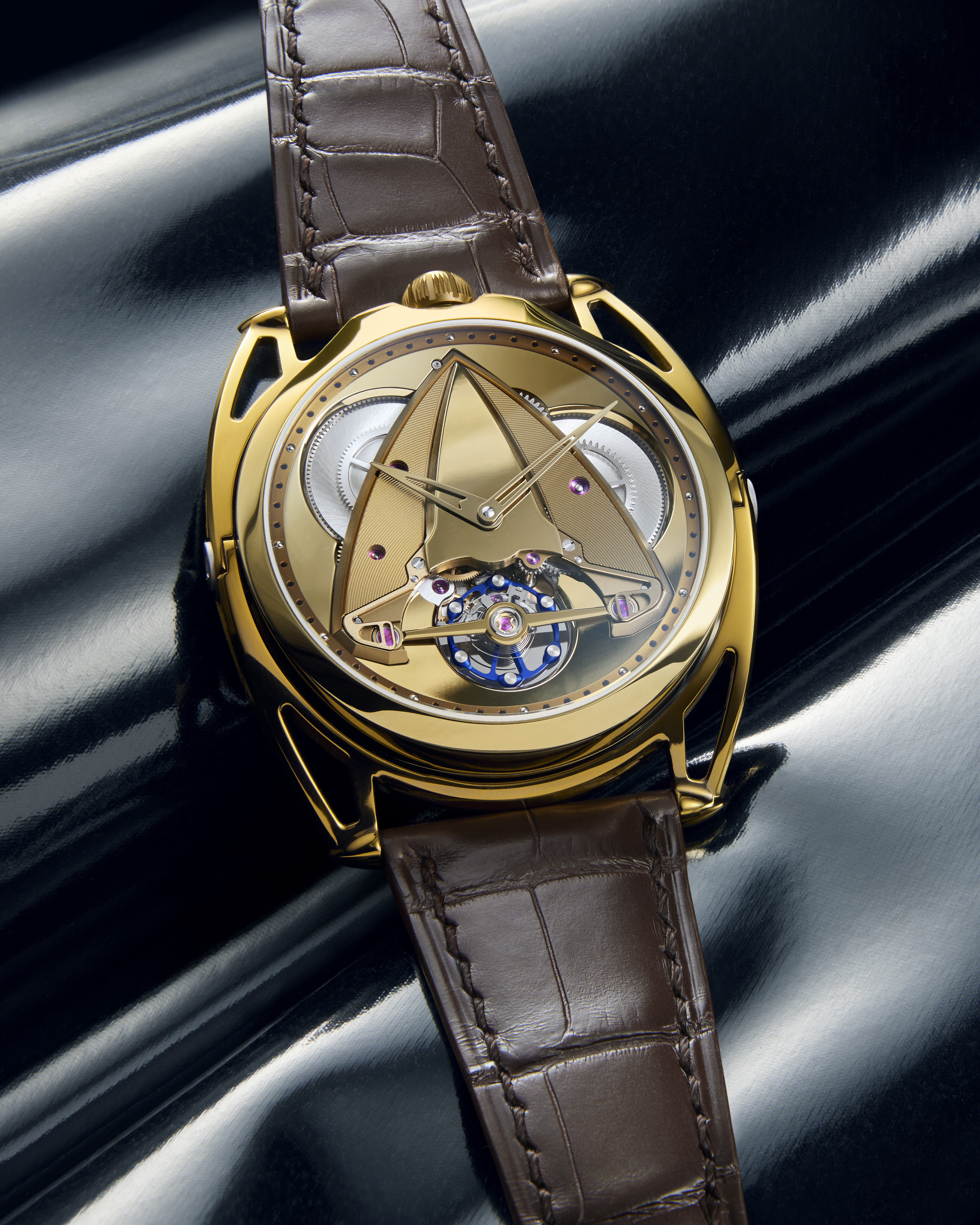 Gold watch with a brown alligator strap, exposed gears, and a triangular face design.