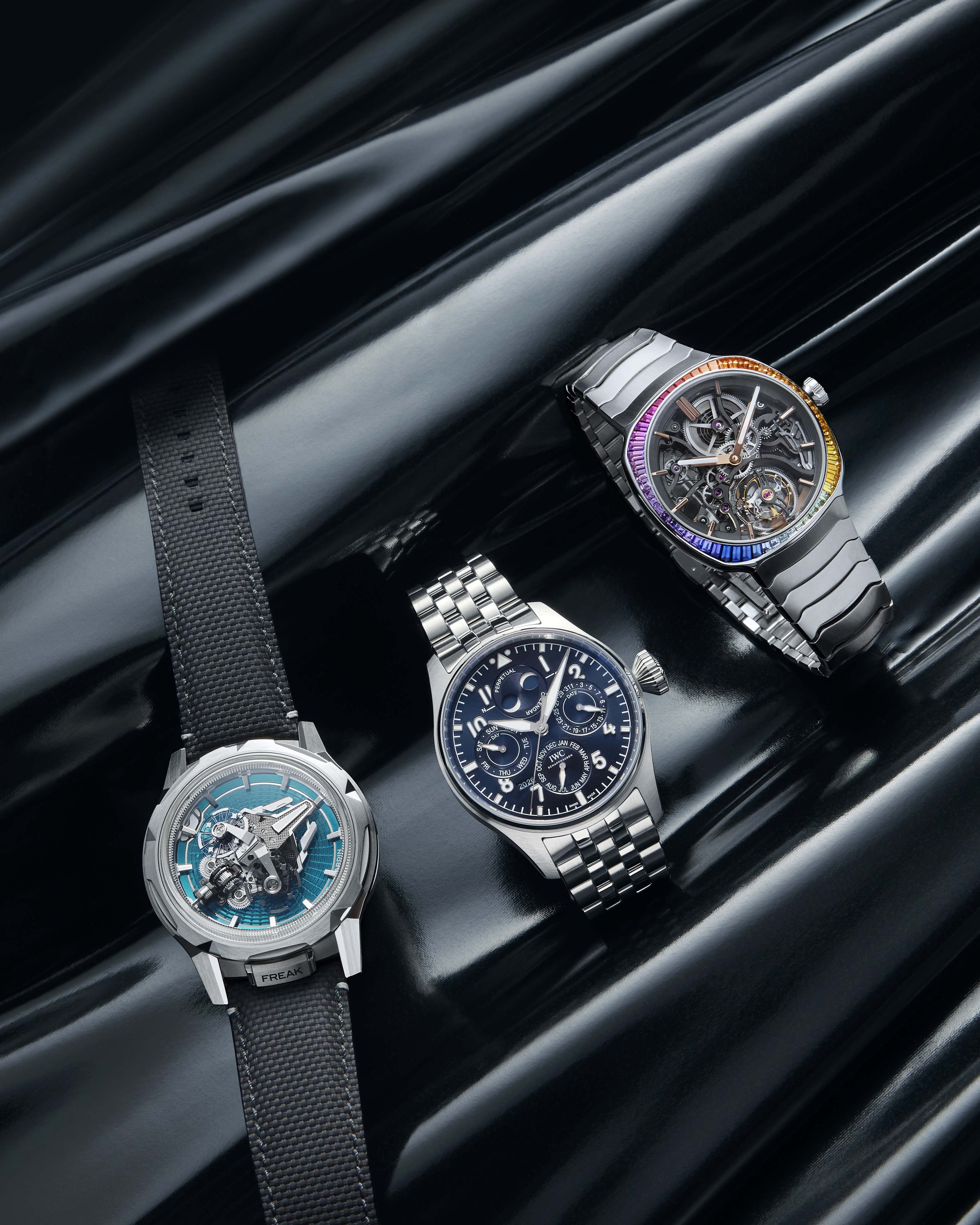 Three luxury watches, two with metal bands and one with a black fabric band, on a reflective black surface.