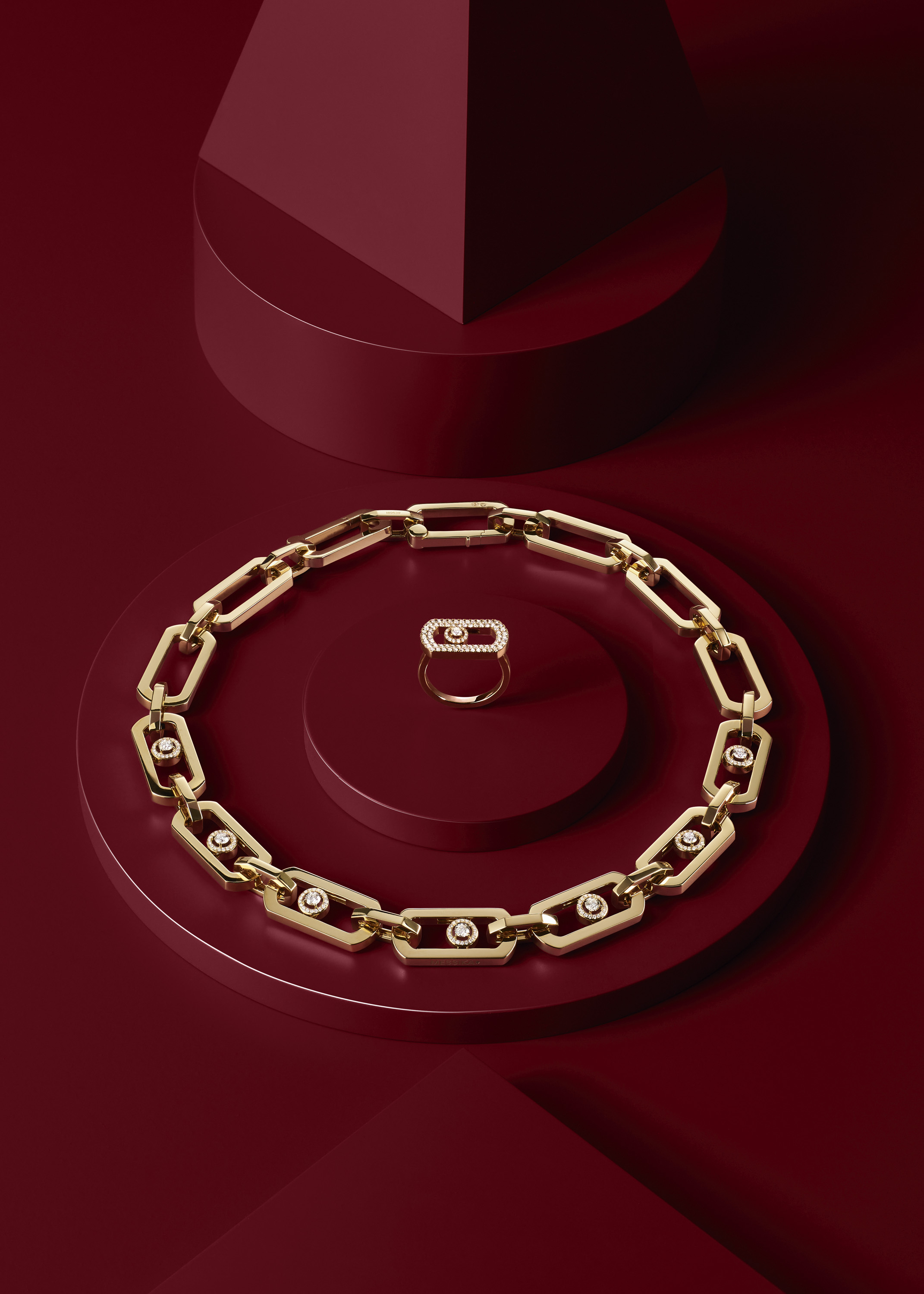 Eine goldene Gliederkette mit Diamantakzenten und ein dazu passender Ring, präsentiert auf geometrischen roten Sockeln.