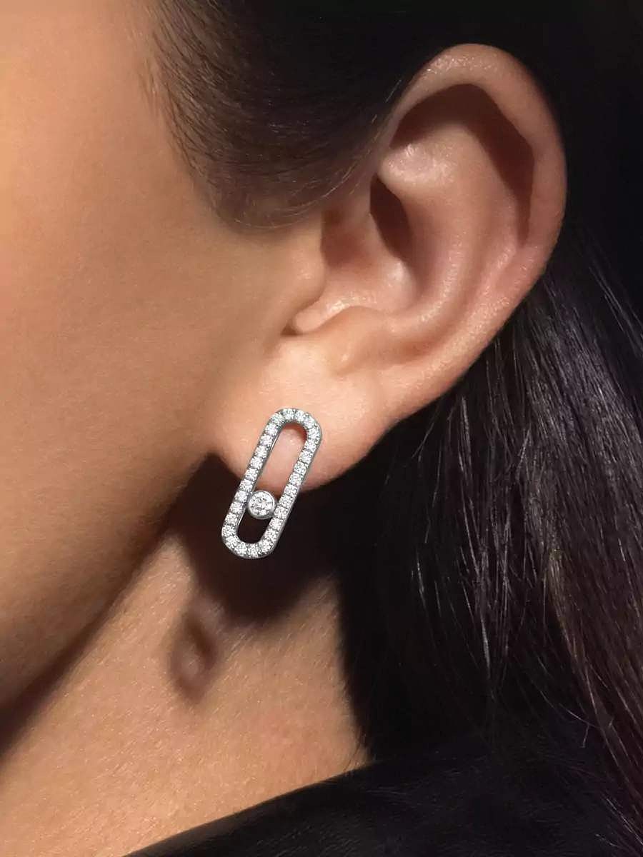 Gros plan sur l'oreille d'une personne portant une boucle d'oreille moderne, oblongue, pavée de diamants, avec un seul diamant flottant au centre.