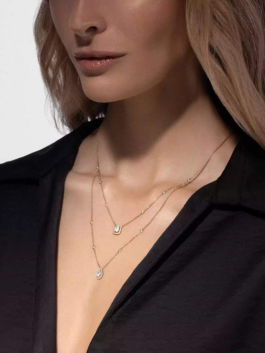 Une femme portant deux colliers en or superposés, l'un avec un pendentif taille émeraude et l'autre avec un pendentif en forme de larme.