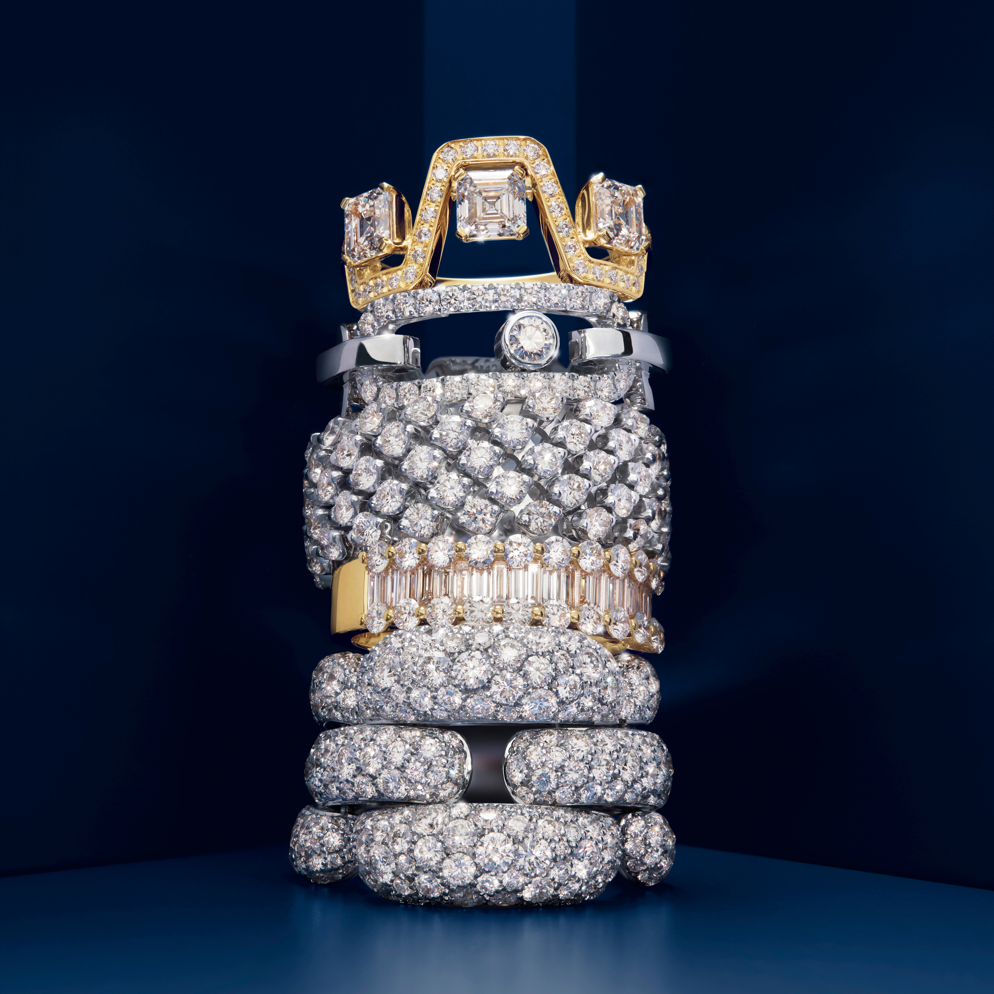 Une haute pile de bagues en diamants et en or sur un fond bleu foncé.
