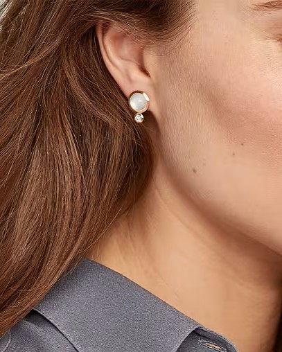A close-up of a person wearing a two-stone gold and pearl earring.