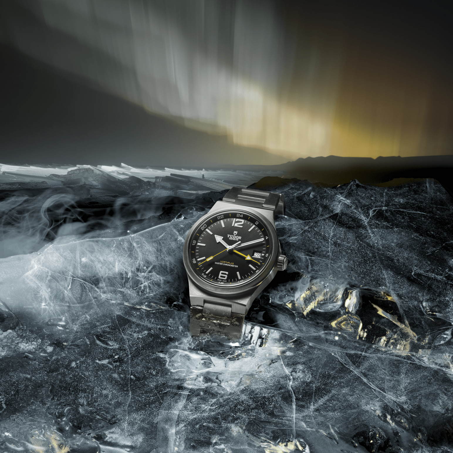 A steel Tudor wristwatch rests on a jagged, icy surface beneath an aurora borealis sky.