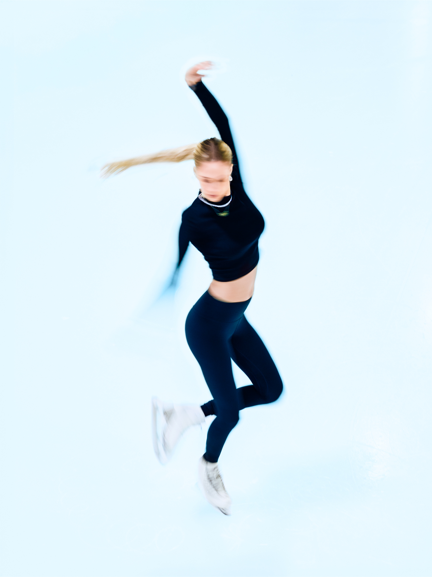 Die verschwommene Gestalt einer blonden Eiskunstläuferin in schwarzer Sportkleidung, die über eine Eisbahn gleitet.