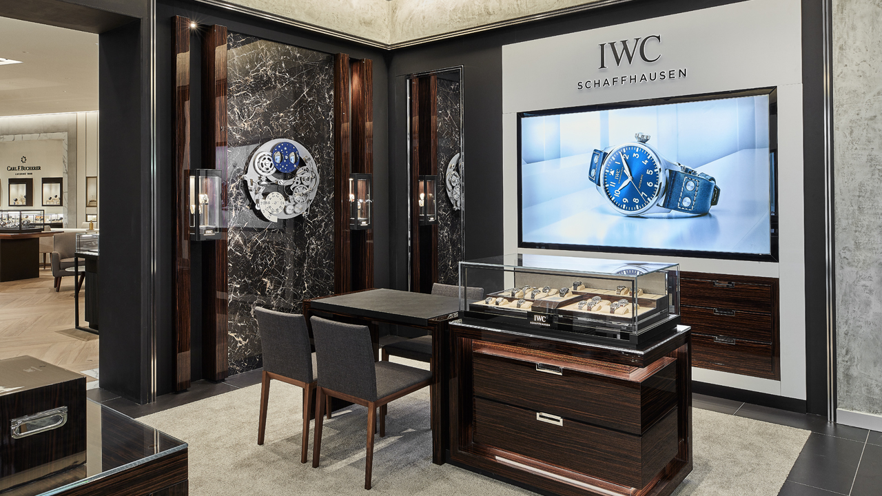 Interior view of an IWC Schaffhausen watch boutique featuring display cases, a digital watch advertisement, and a seating area.