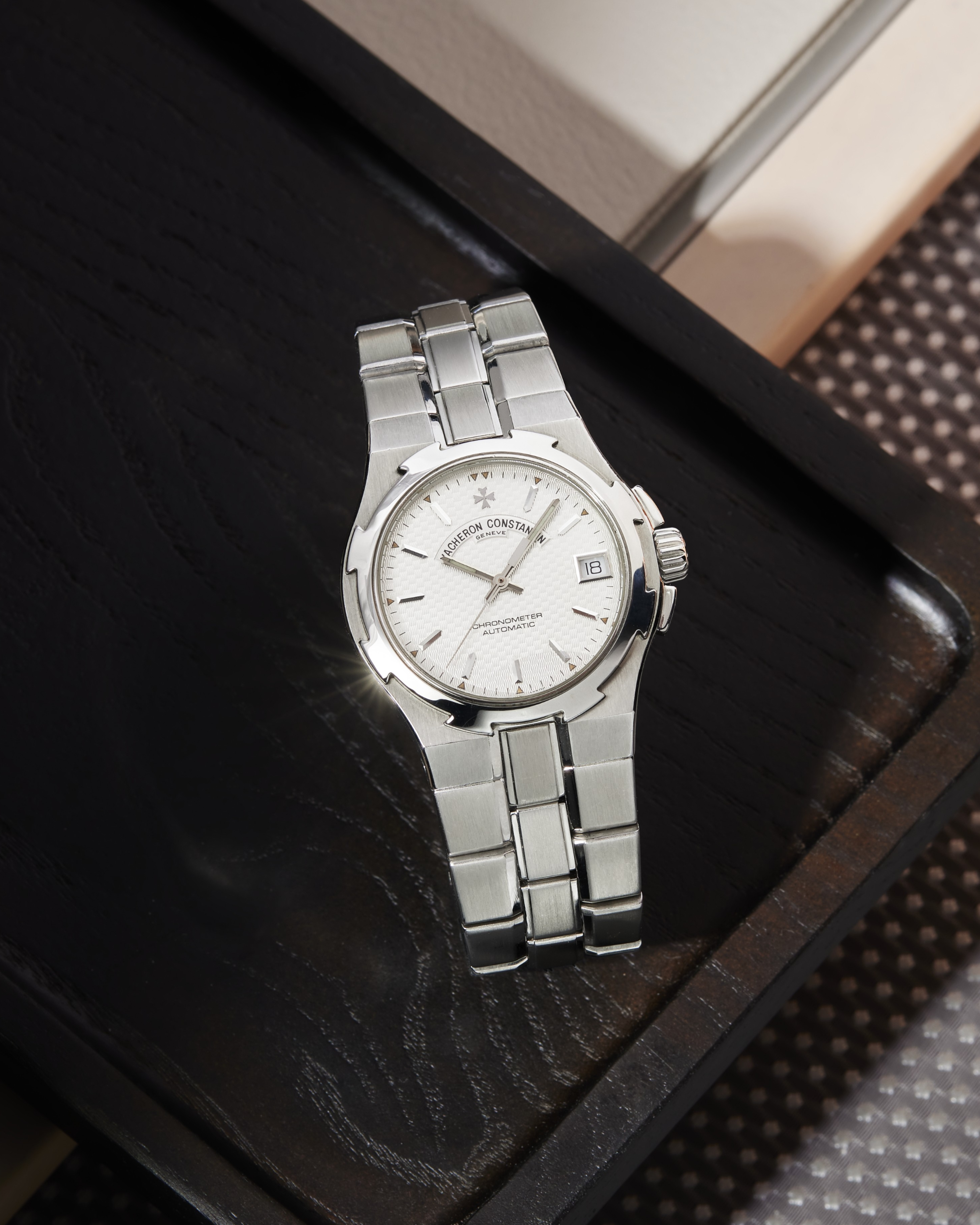 Eine Vacheron Constantin Armbanduhr aus Edelstahl liegt auf einem dunklen Holztablett.