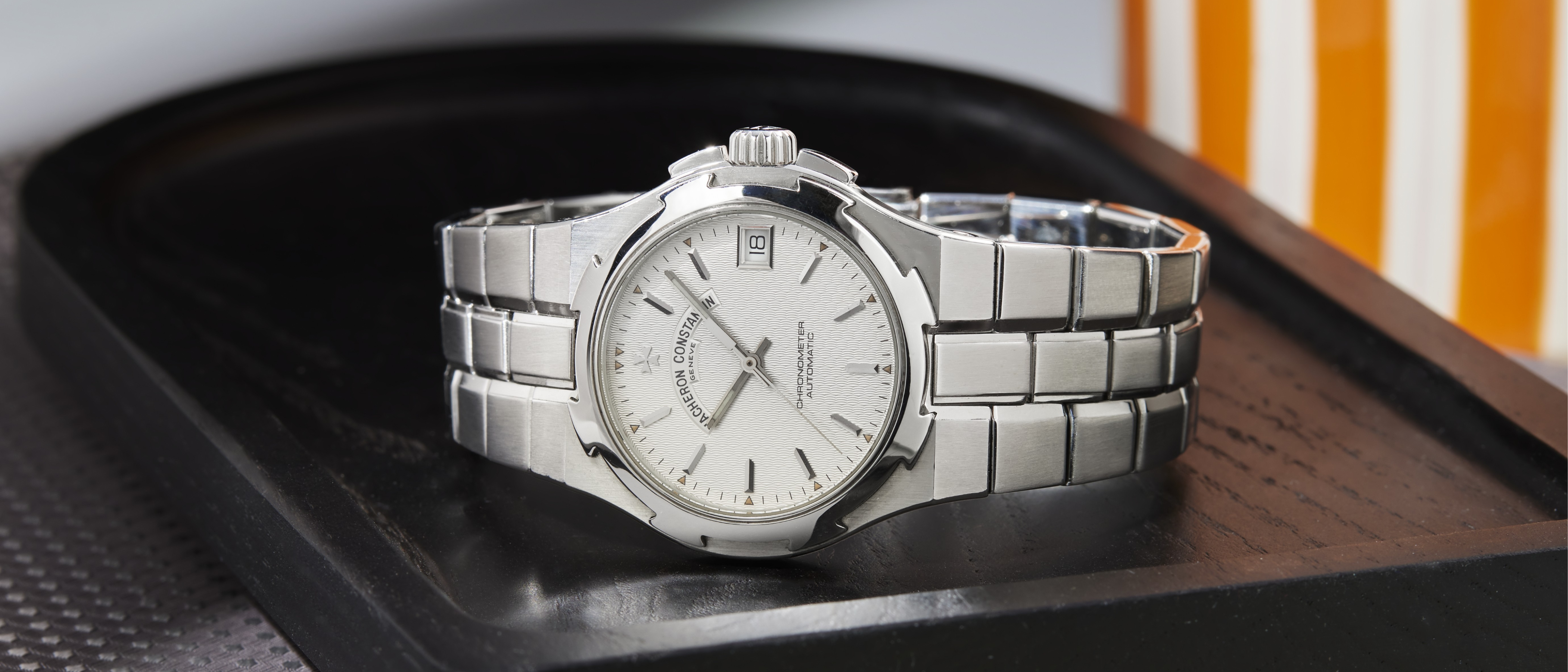 Eine Vacheron Constantin Armbanduhr mit silbernem Zifferblatt und Stahlarmband liegt auf einem dunklen Tablett.