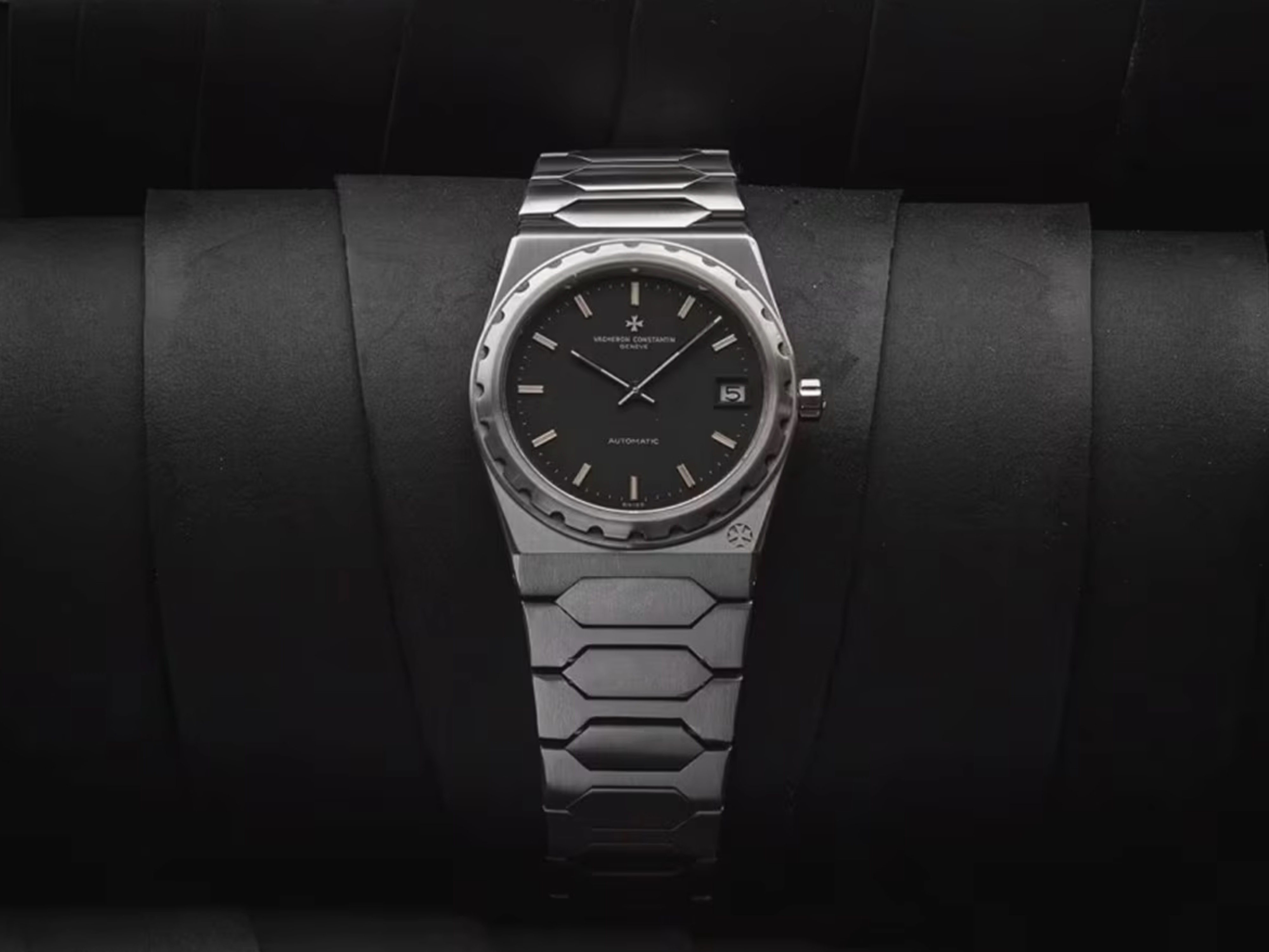 Eine silberne Vacheron Constantin Armbanduhr mit schwarzem Zifferblatt und integriertem Metallarmband, vor dunklem Hintergrund.