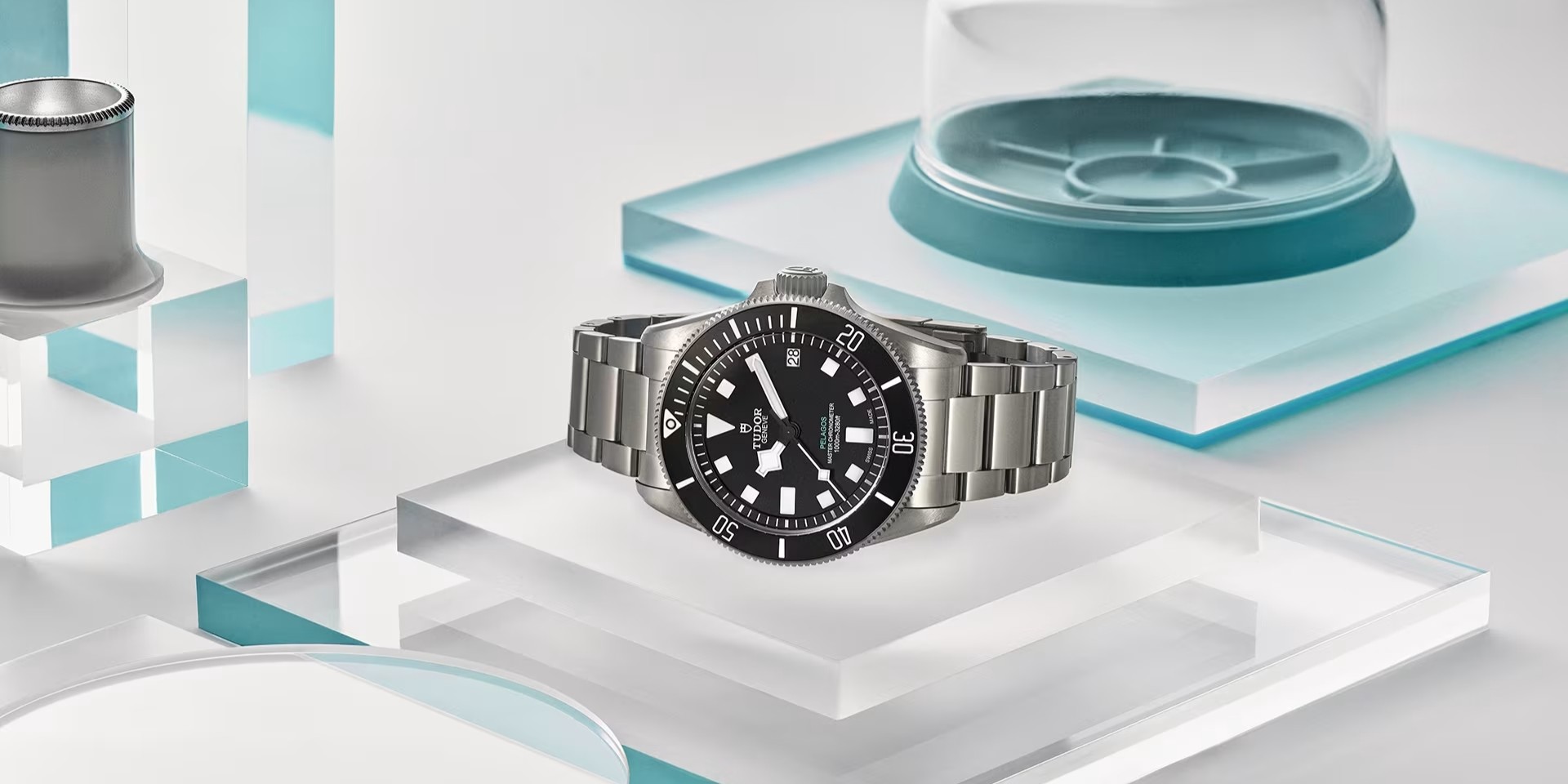 Deux montres TUDOR Pelagos avec cadrans bleu foncé et bracelets en tissu, présentées côte à côte sur un fond d'inspiration marine avec des cordages nautiques et des équipements métalliques. Le design robuste et les caractéristiques de qualité professionnelle soulignent l'engagement de Tudor pour la durabilité et la précision en milieu sous-marin.
